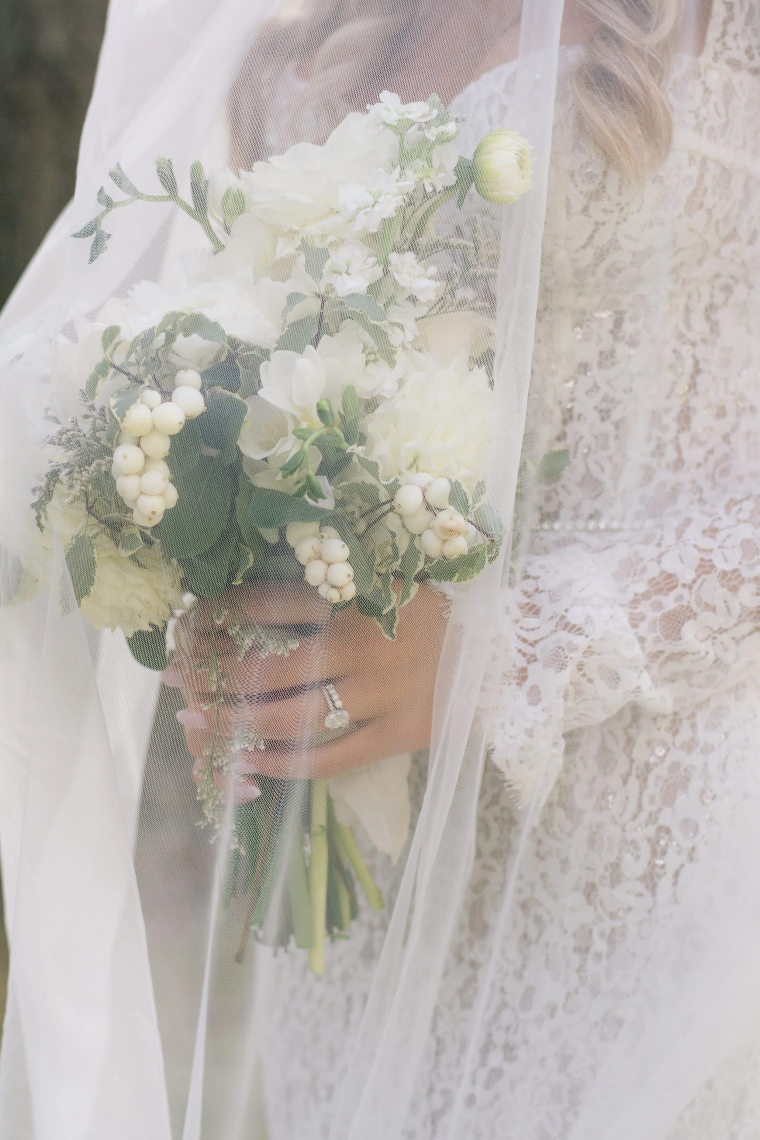 Elegant bridal bouquet with white roses and berries held by a bride in a long-sleeve lace dress, captured in a bright and airy photography style.