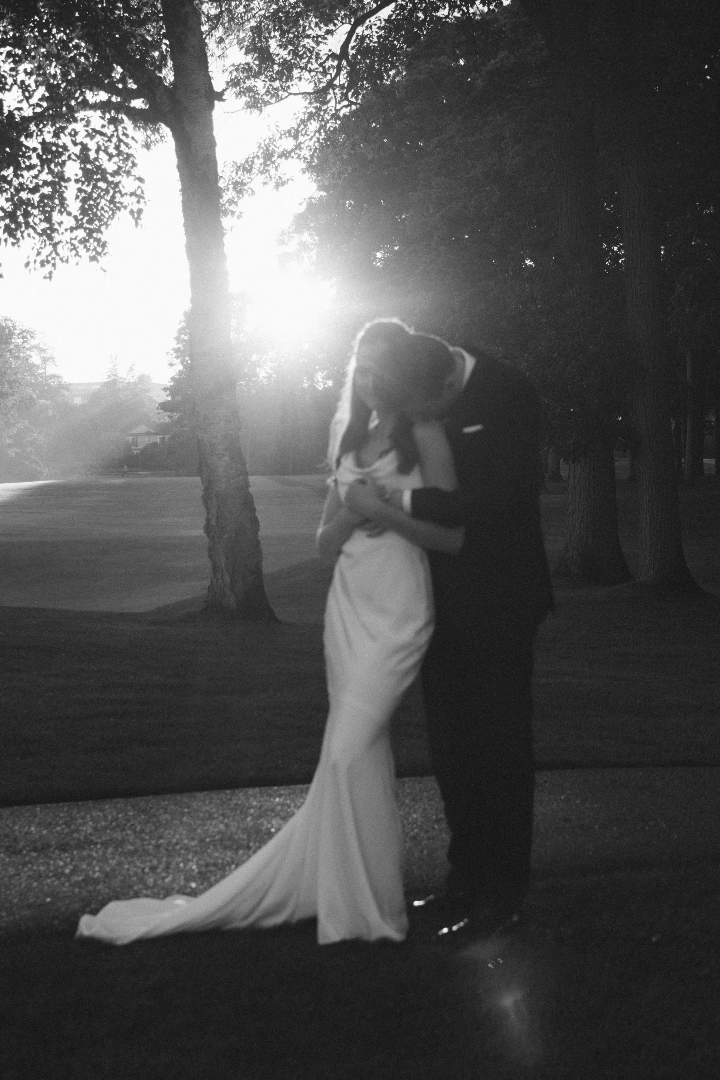 Romantic silhouette of bride and groom embracing outdoors with sunlight streaming through trees