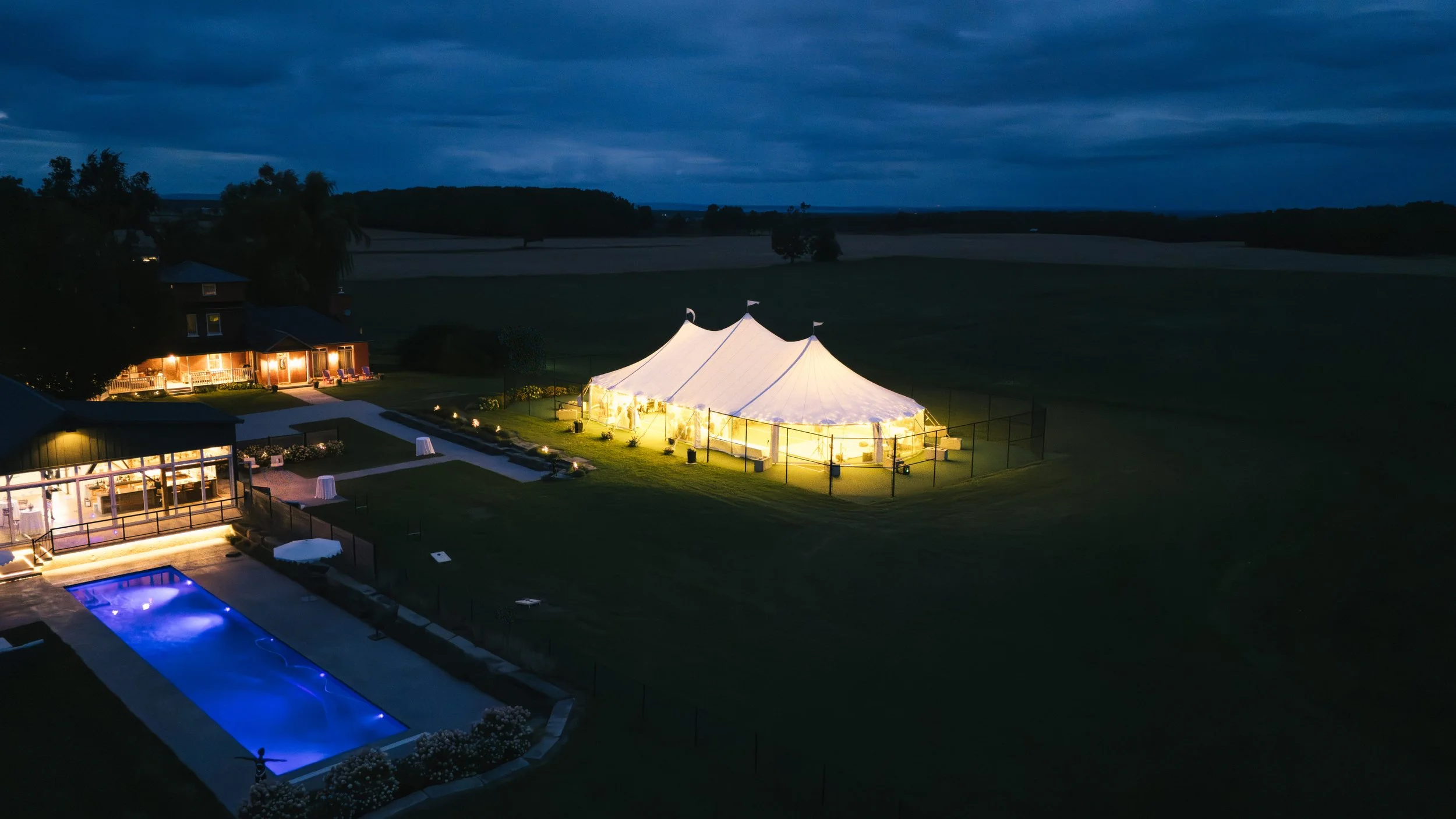 Aerial view of an outdoor sailcloth tent wedding reception glowing at dusk on a private estate