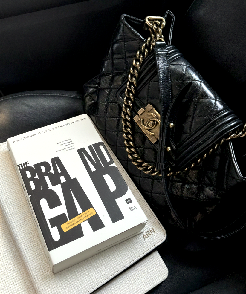 The brand gap book ontop of stacked ipad and computer in the front seat of a car with Chanel handbag