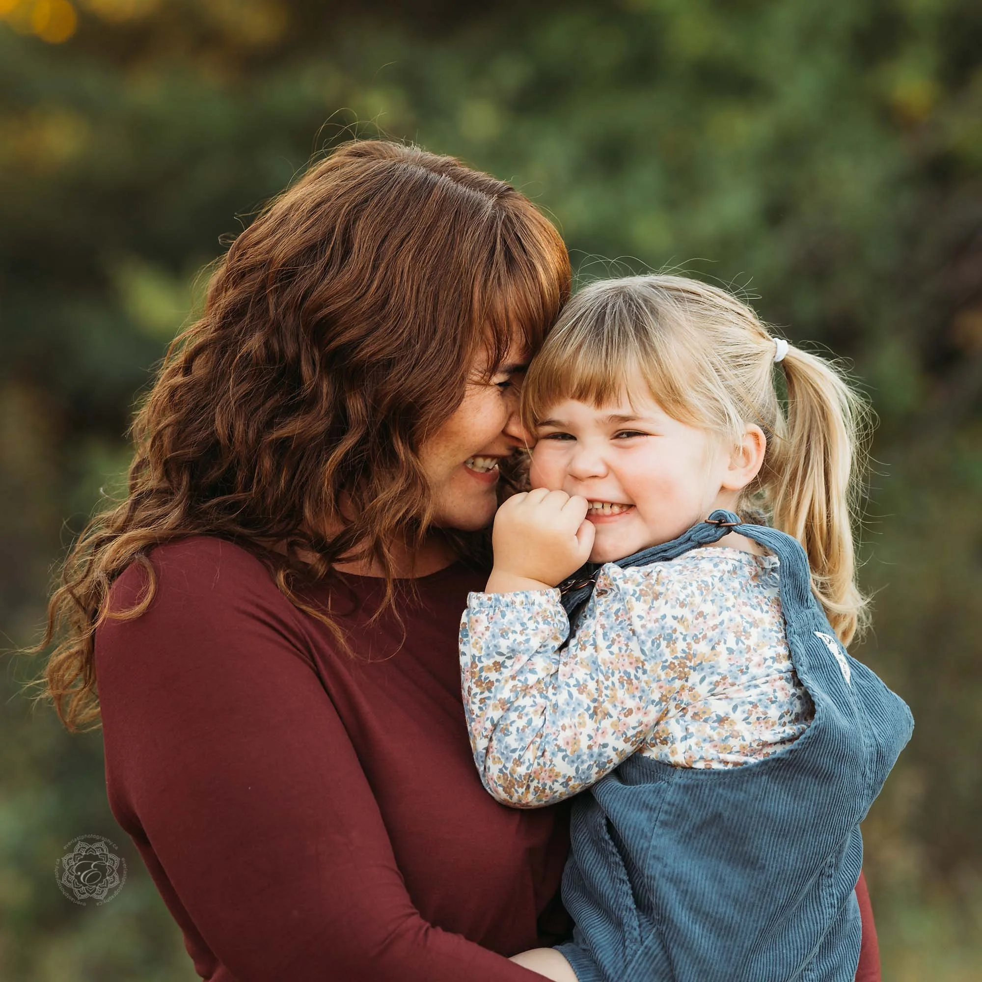 Mother and small daughter snuggling tightly with smiles in an outdoor setting with beautiful soft light