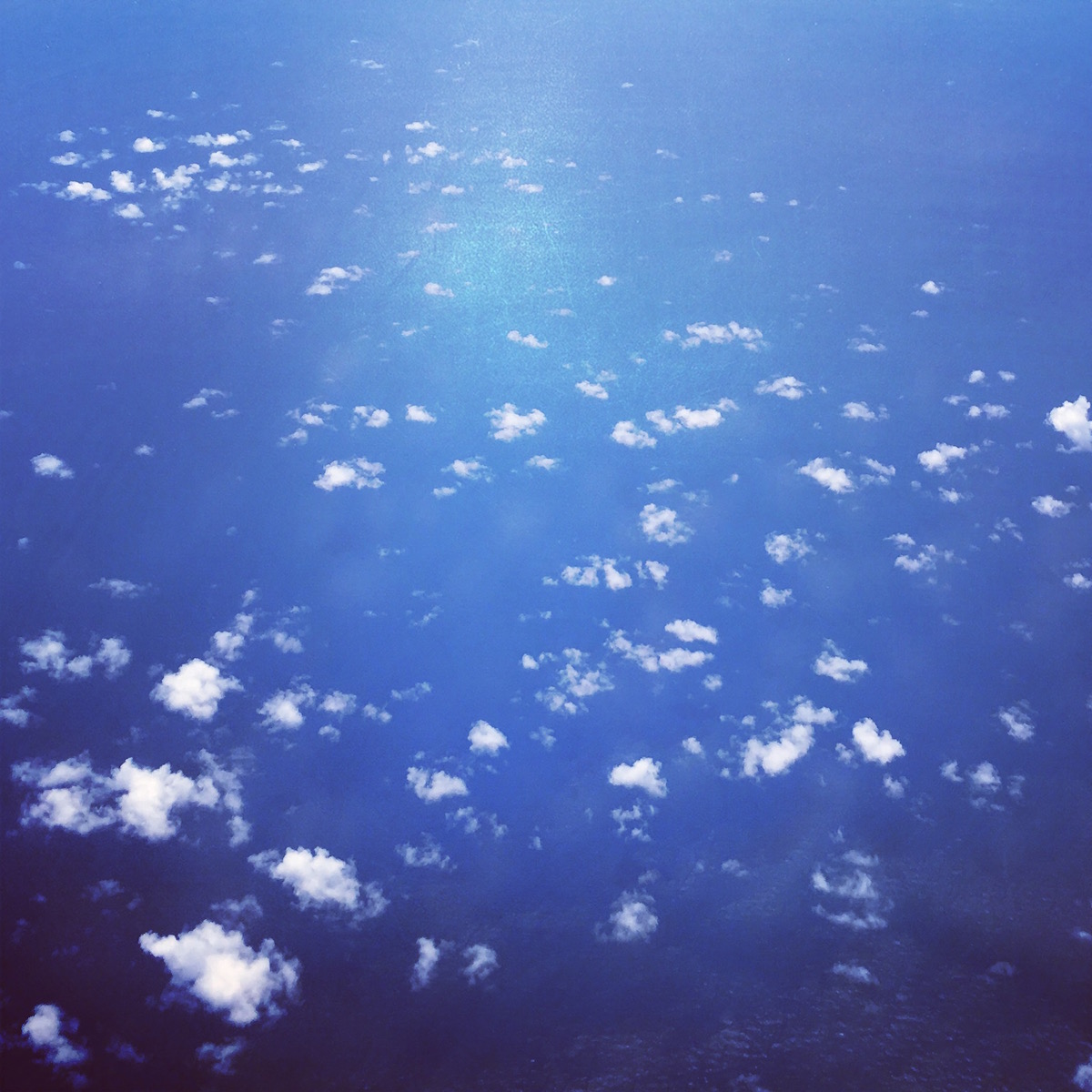 The sea is sparkling blue below, and a smattering of clouds hang like powdered sugar in the otherwise clear sky below, stretched out far as the eye can take in.