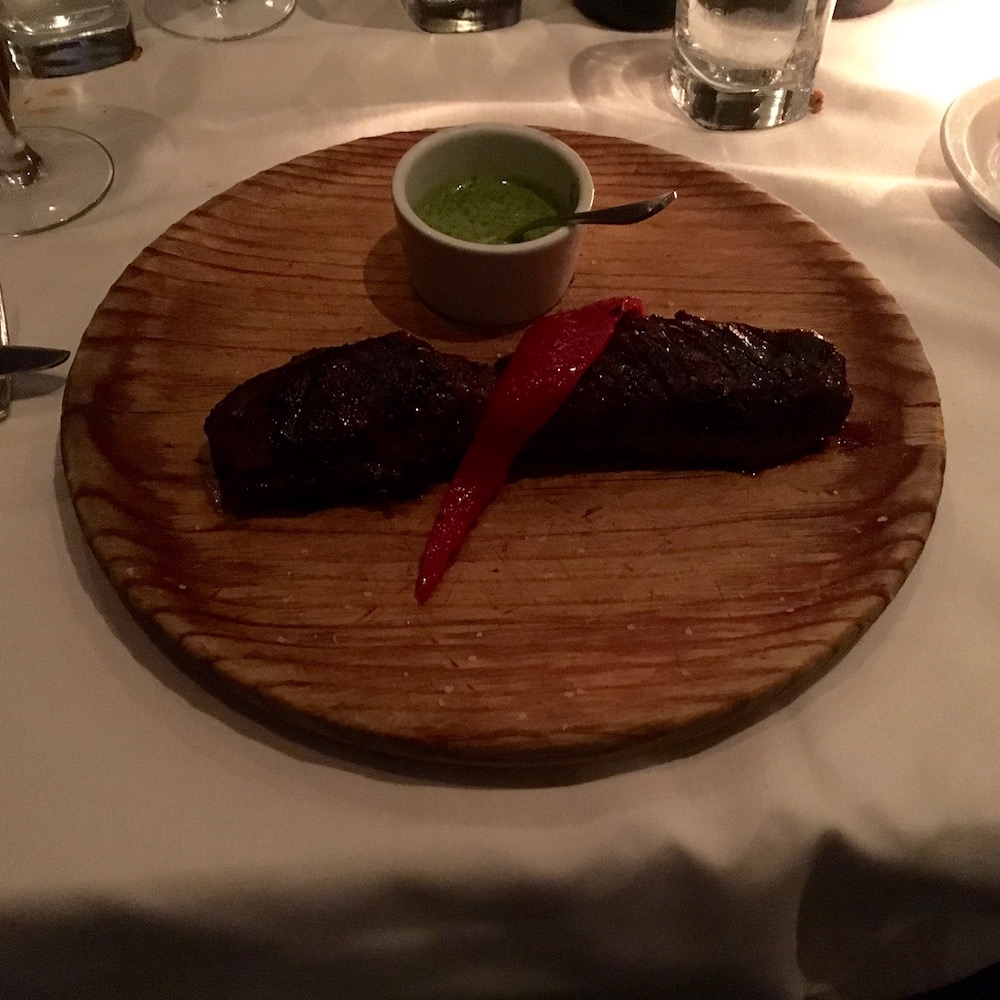 Simple elegance. Our preferred Vacio a la Gaucho (Hangar Steak) is served on a wooden plate with chimichurri sauce and a simple garnish.