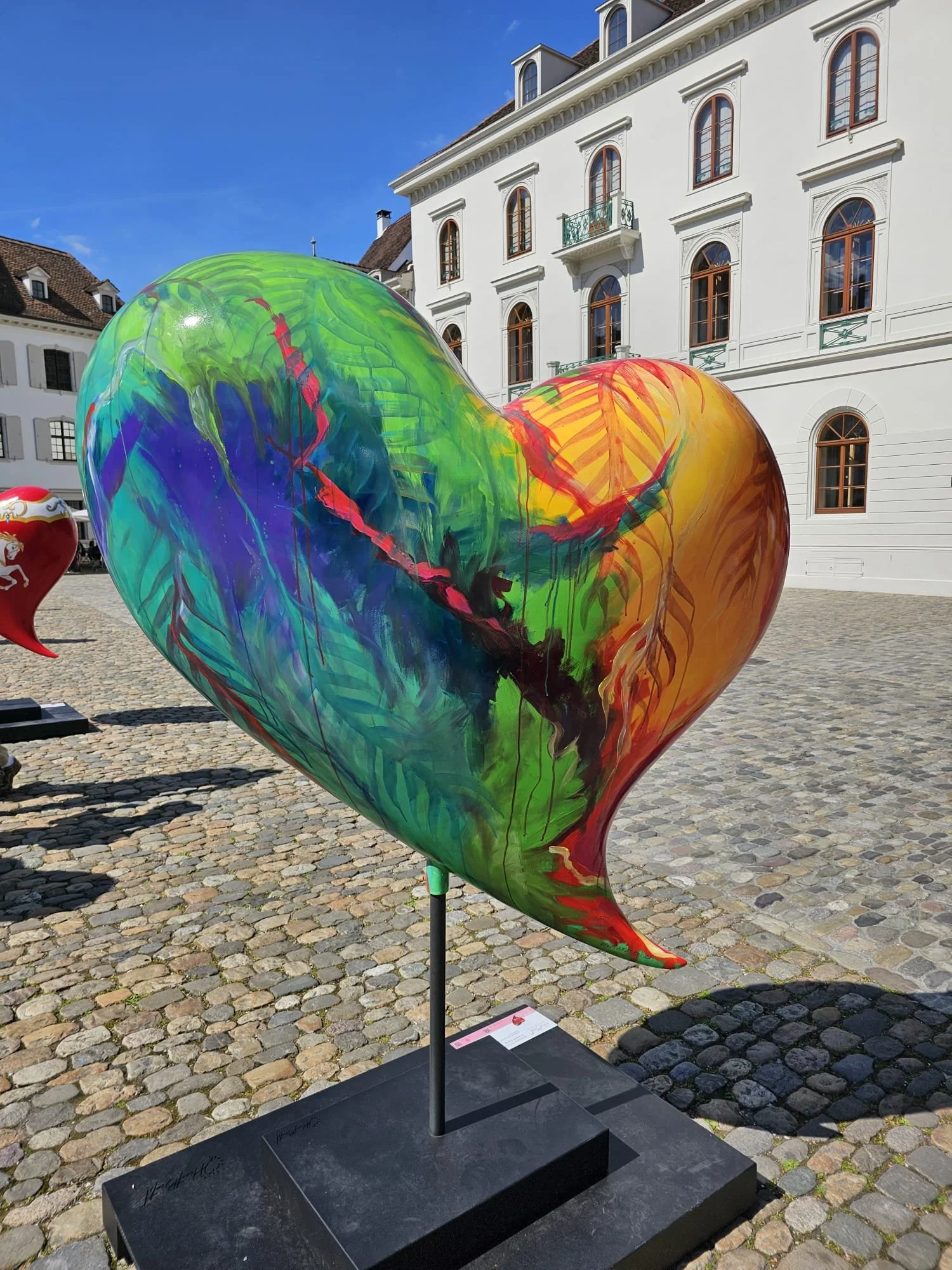  HeartBeats . 2025 . BananaTukan auf Herz . Hinten (Foto vom Münsterplatz Basel) 