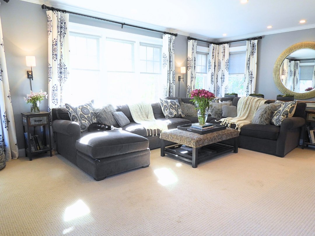 Cozy stylish family room design featuring sectional sofa patterned curtains sconces and round oversized mirror