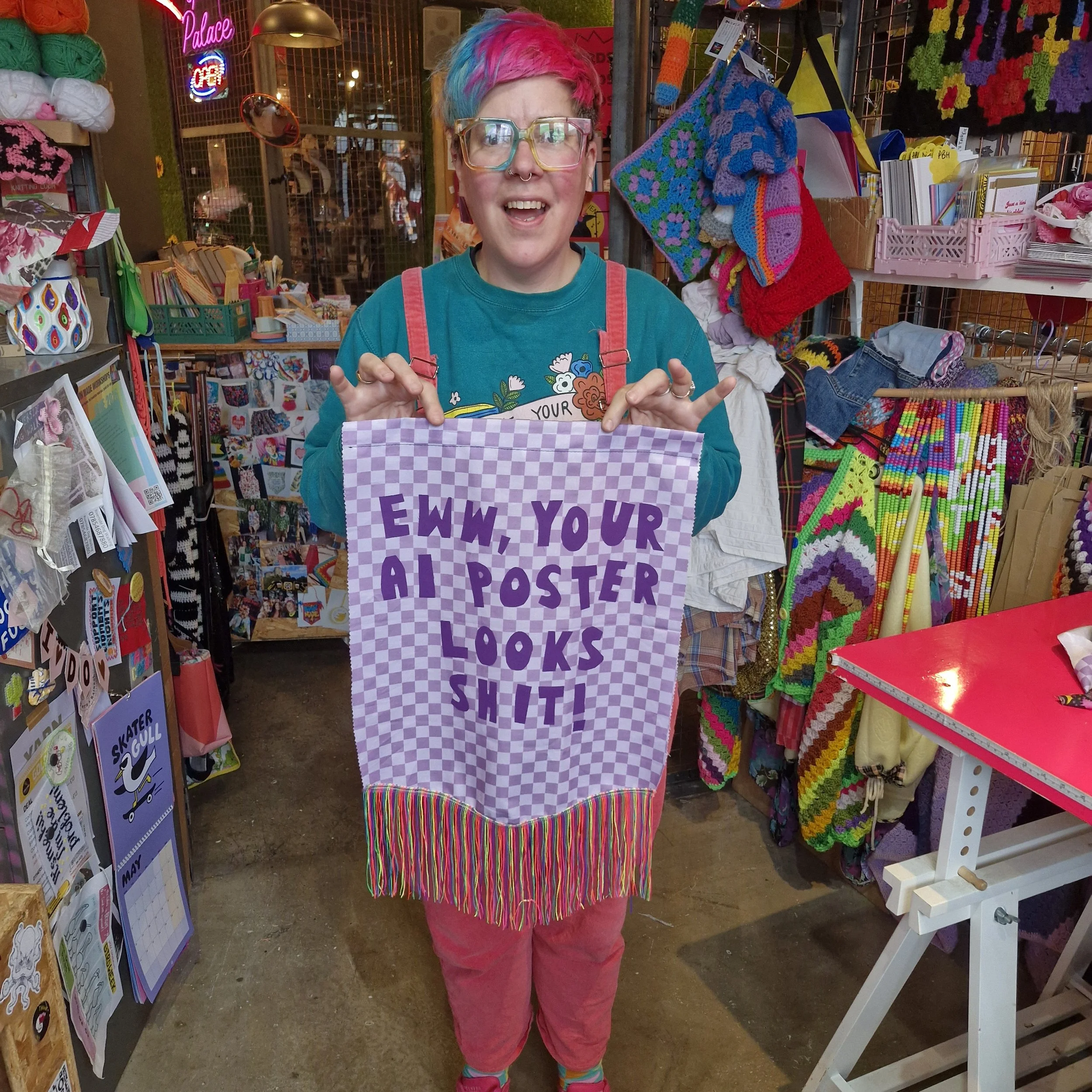 A person with colourful hair holding a hand made banner which reads: Eww, Your AI Poster Looks Shit