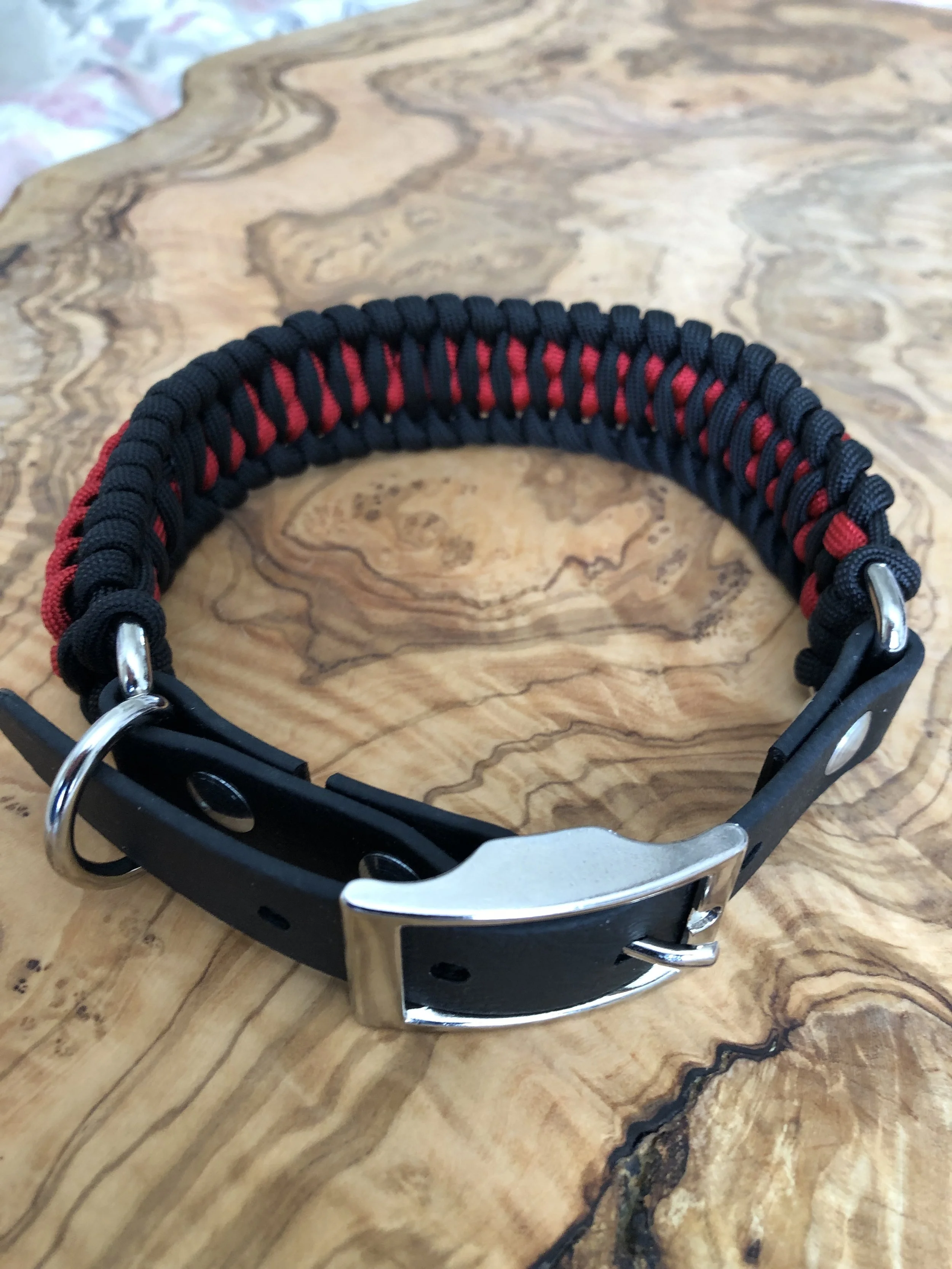 black and red paracord dog collar with a 3/4” biothane adapter. It is adjustable from 13.5" to 16" and is 1.5" wide, pictured on a light wood table