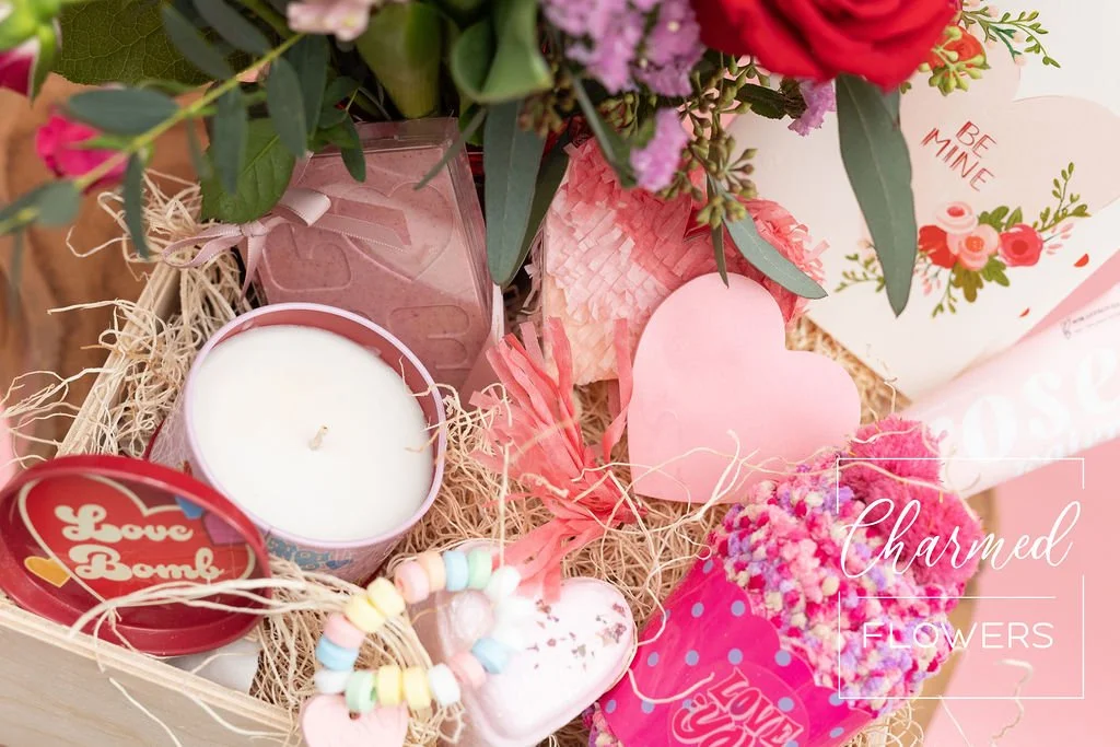 The Deluxe Love Bomb Bundle features fresh flowers in a vase, bath and body products, some treats, and a heart pinyatta