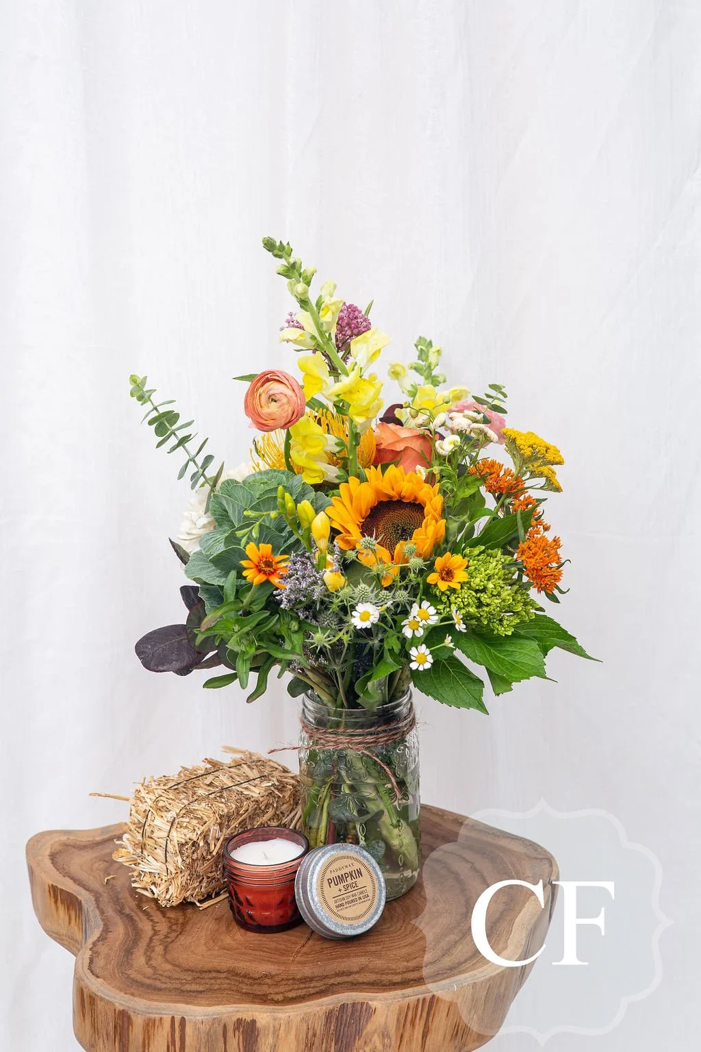 Cheerful Yellow Vase Flower Arrangment beside a Seasonal Candle and Decrative Hay Bail
