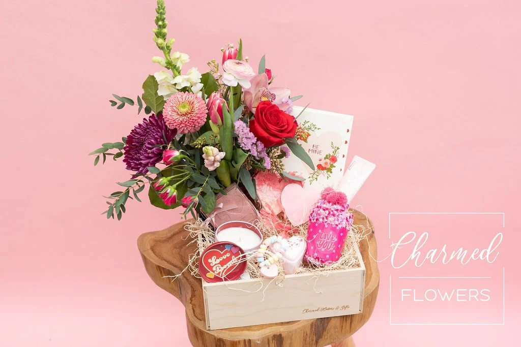 The Deluxe Love Bomb Bundle features fresh flowers in a vase, bath and body products, some treats, and a heart pinyatta