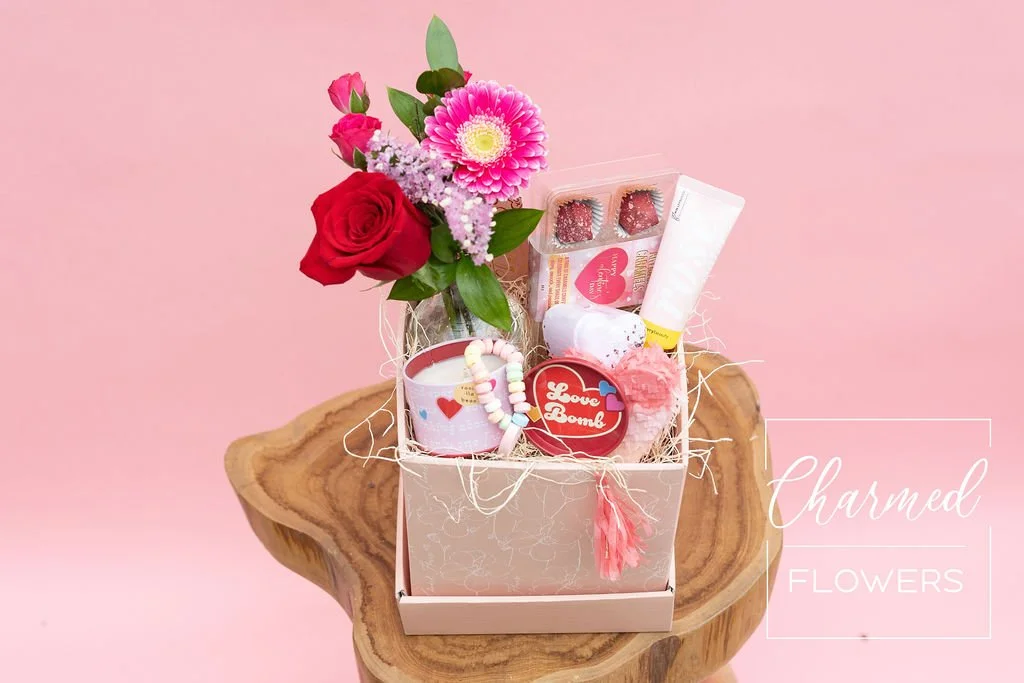 The petite Love Bomb Bundle features fresh flowers in a vase, bath and body products, some treats, and a heart pinyatta