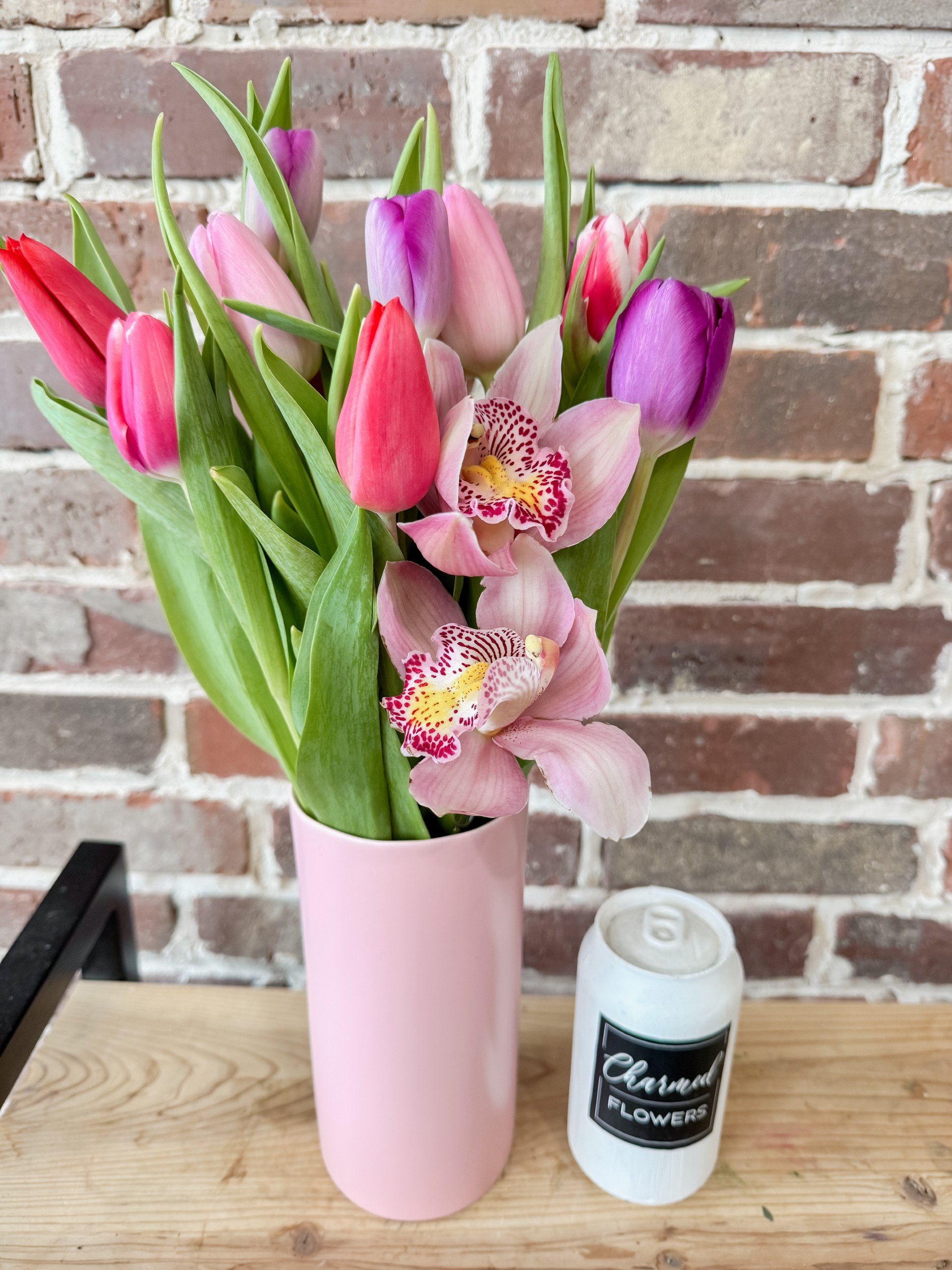 Tulips and Orchids in Pinks and Purples arranged in a tall pink vase