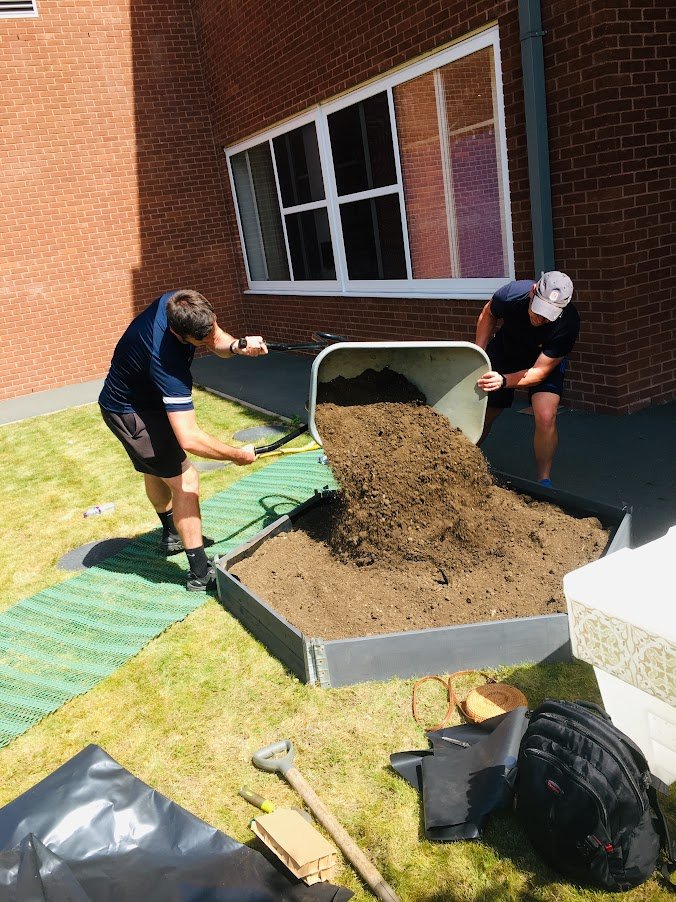 2 volunteers pouring soil into a raised bed planter.JPG
