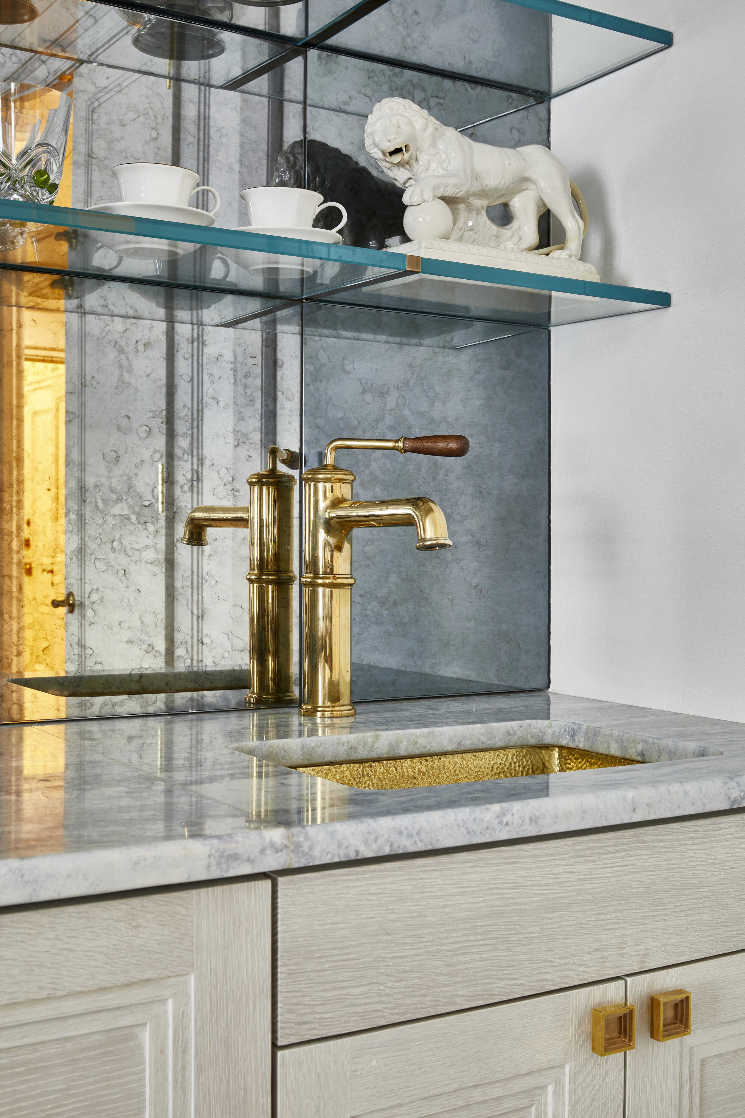 Custom millwork, mirrored wall, and floating glass shelves by Leone Construction Canteen bar faucet by Waterworks Hammered brass bar sink by Alno Inc