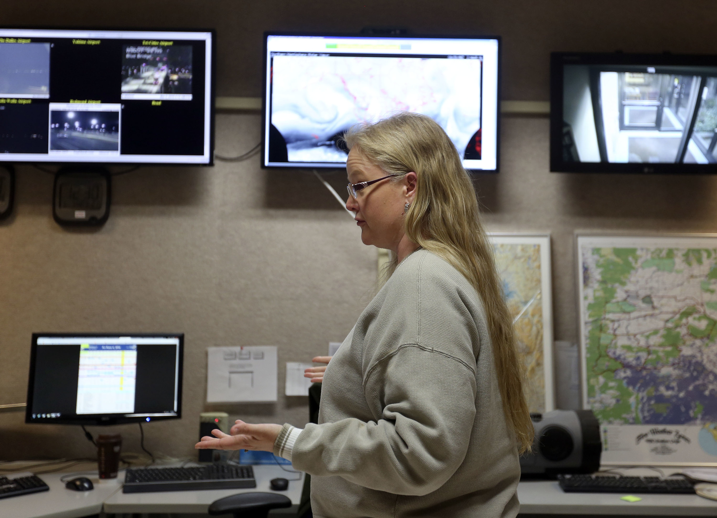   Various weather maps and computer screens of satellite and radar images frame meterologist Mary Wister as she talks to a co-worker during an overnight shift at the National Weather Service in Pendleton. With two decades in the field, Wister has see