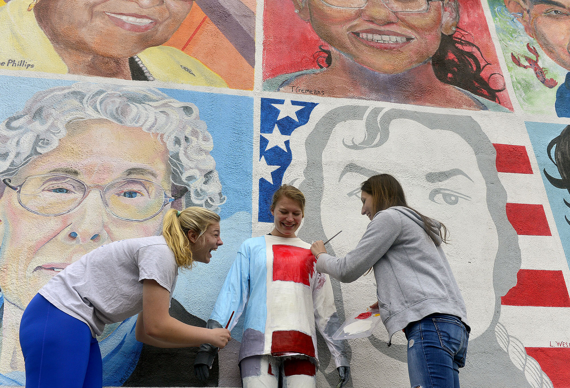  Connecticut College sophomores Emily Ehler, right, and Emily Senatore, left, laugh as they paint classmate Caitlyn Teare, center, into the "One Place Many Cultures" mural on Friday, May 12, 2017, as part of their final for a color theory class "Deco