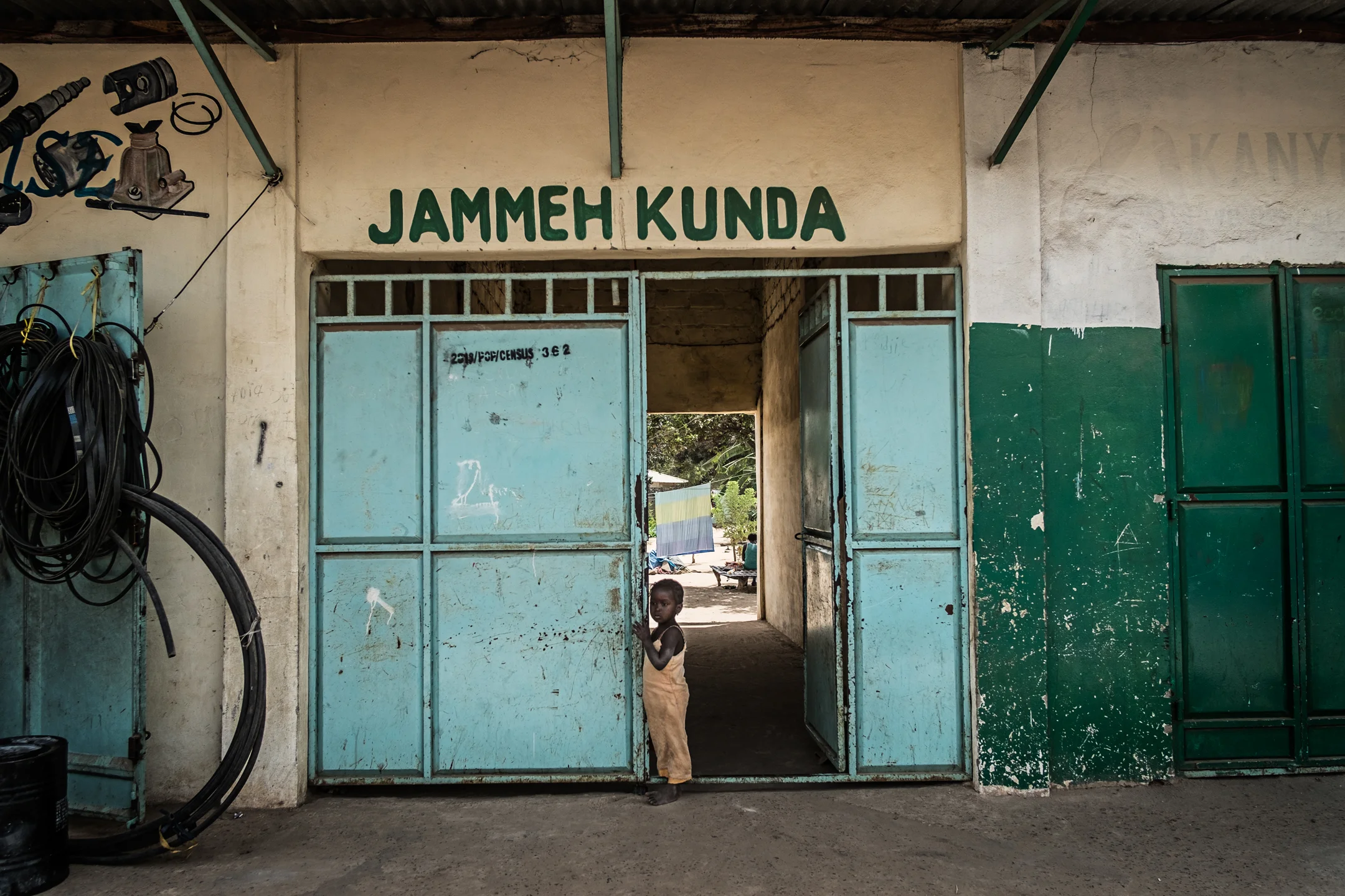 A young child at the entrance of a green compound between Banjul airport and the town of Lamin, The green colour painted is representing the former president Jammeh ´s party APRC (Alliance for Patriotic Reorientation and Construction). “ If you look at all the shops and other building in most towns you will see this green colour. This green is a representation of Jammeh's party and this means that he had shares in all of these businesses that this colour is painted on. If you refused to deal with him, he made it to difficult for a person to open his own business and even shut you down at times. He even created kilometres of compounds where he had people living there for free but also labouring for free, he would take the profit of what was produced there.” Shares a 39 years old Mechanic. 