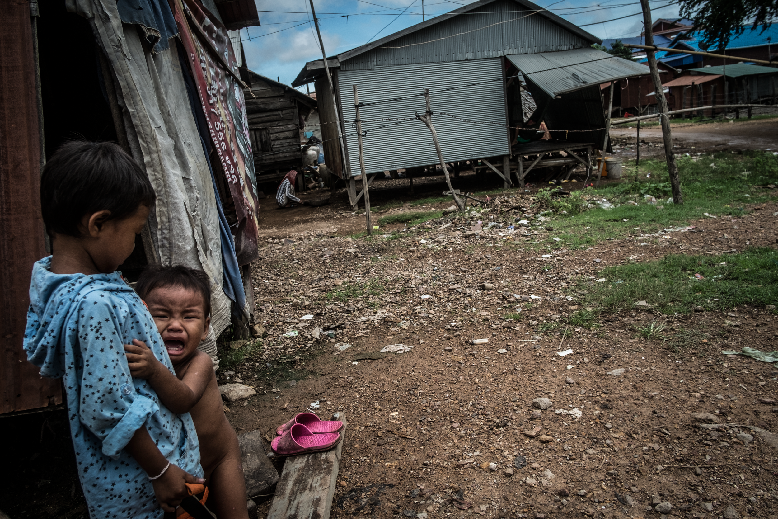 A child crying in the arms of his brother in the slums of Siem Reap Province, Cambodia. / All rights reserved © Clément Martz.