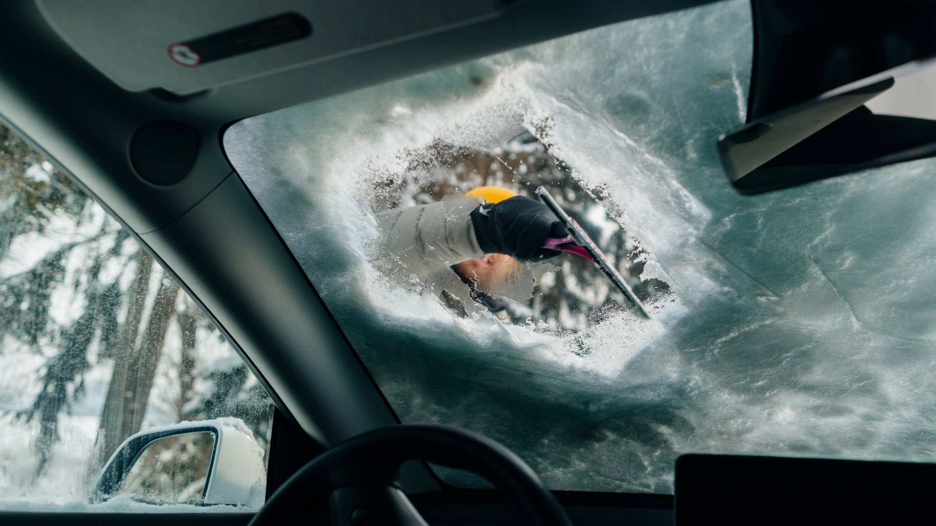Showing a man defrosting a car window  with the point of view from inside the car