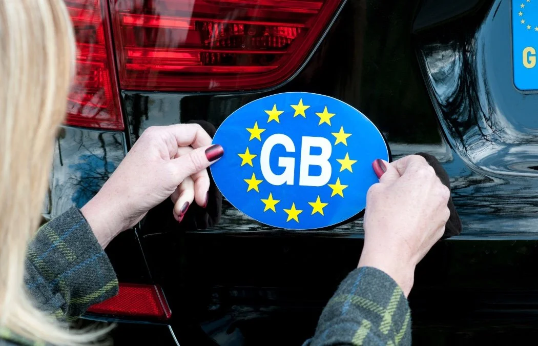 a woman placing a GB sticker to the back of a car