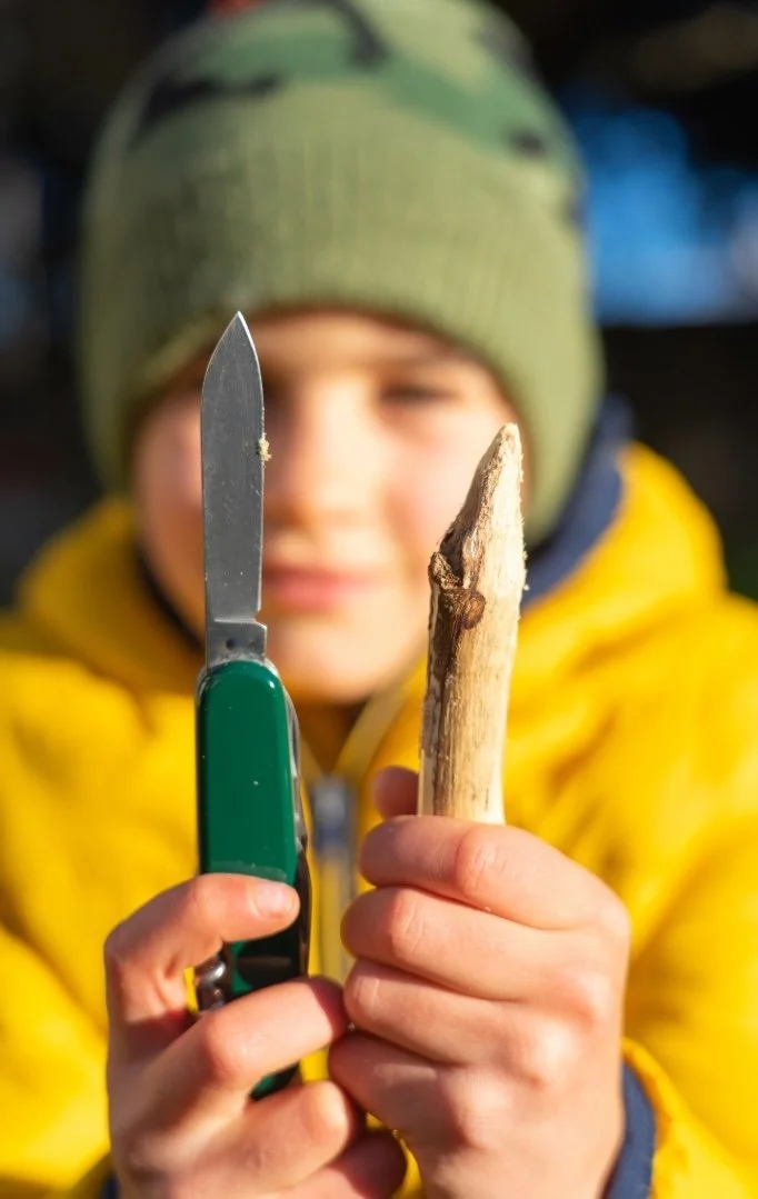 a boy holding up a whittled stick and the pocket knife he used