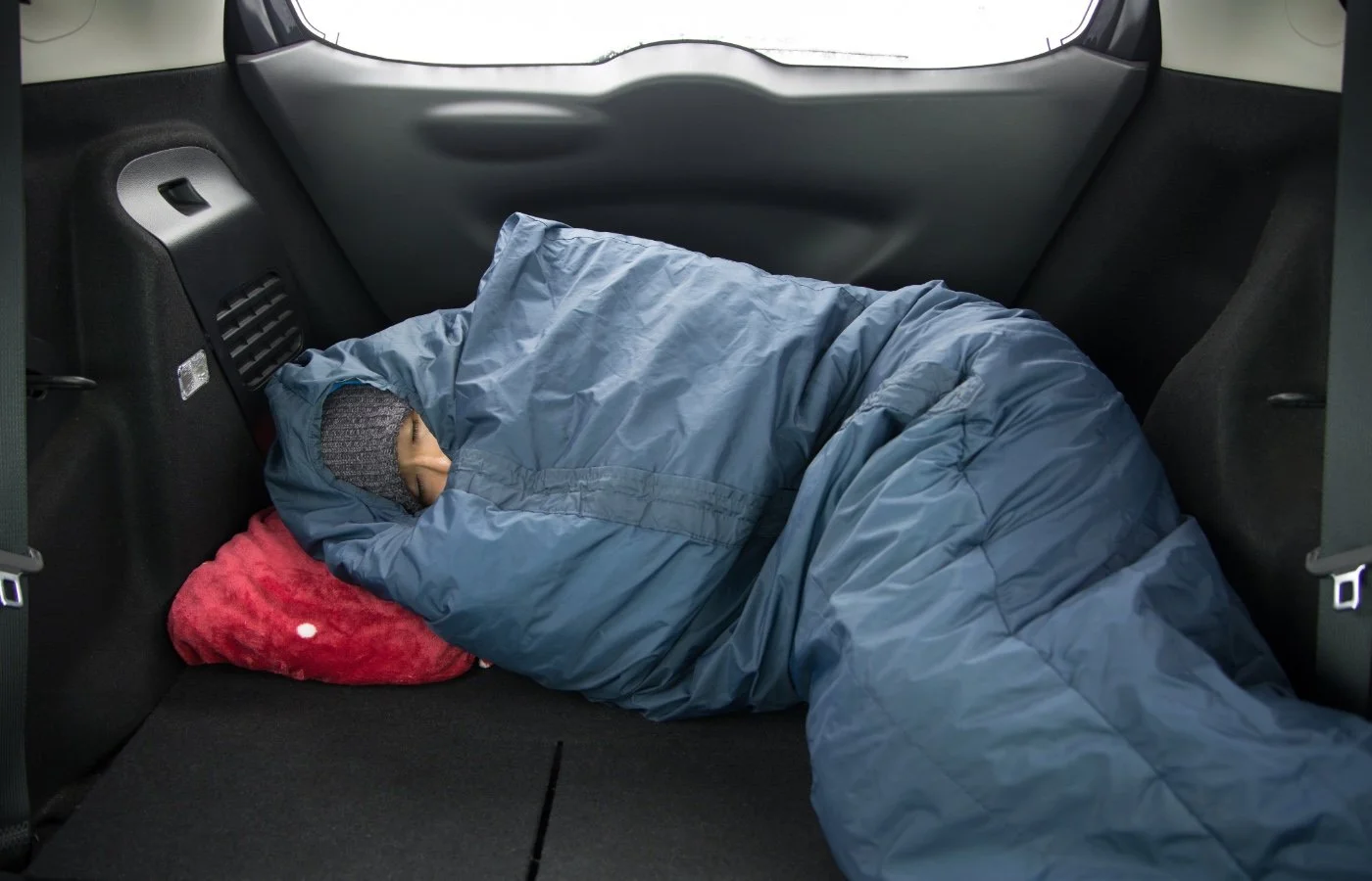 a woman in a sleeping bag in the back of a large car