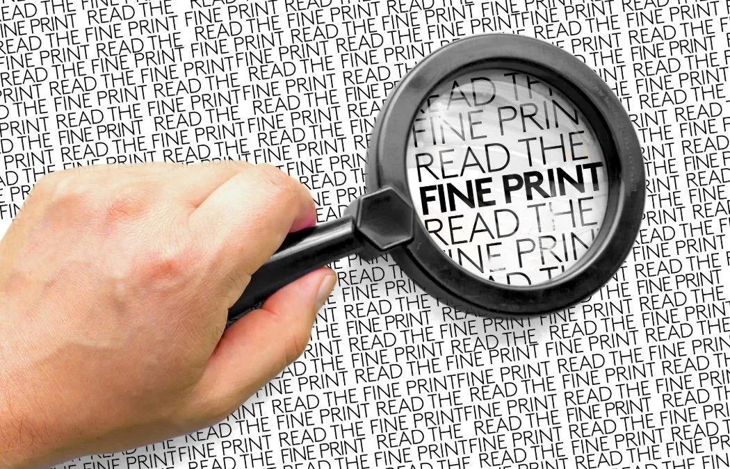 a hand holding a magnifying glass over small print that reads 'Read the fine print'