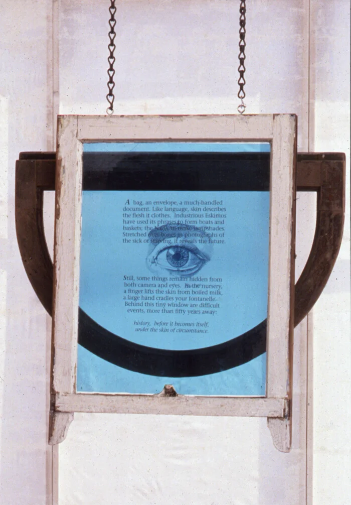 Under ... detail. Text on this window:
A bag, an envelope, a much-handled document. Like language, skin describes the flesh it clothes. Industrious Eskimos have used its phrases to form boats or baskets; the Nazis, to make lampshades. Stretched over bones in photographs of the sick or starving, it reveals the future. Some things, though, remain hidden from both camera and eyes. In the nursery, a finger lifts the skin from boiled milk; a large hand cradles your fontanelle. Behind this tiny window are difficult events, still fifty years away. History, before it becomes itself, under the skin of circumstance.