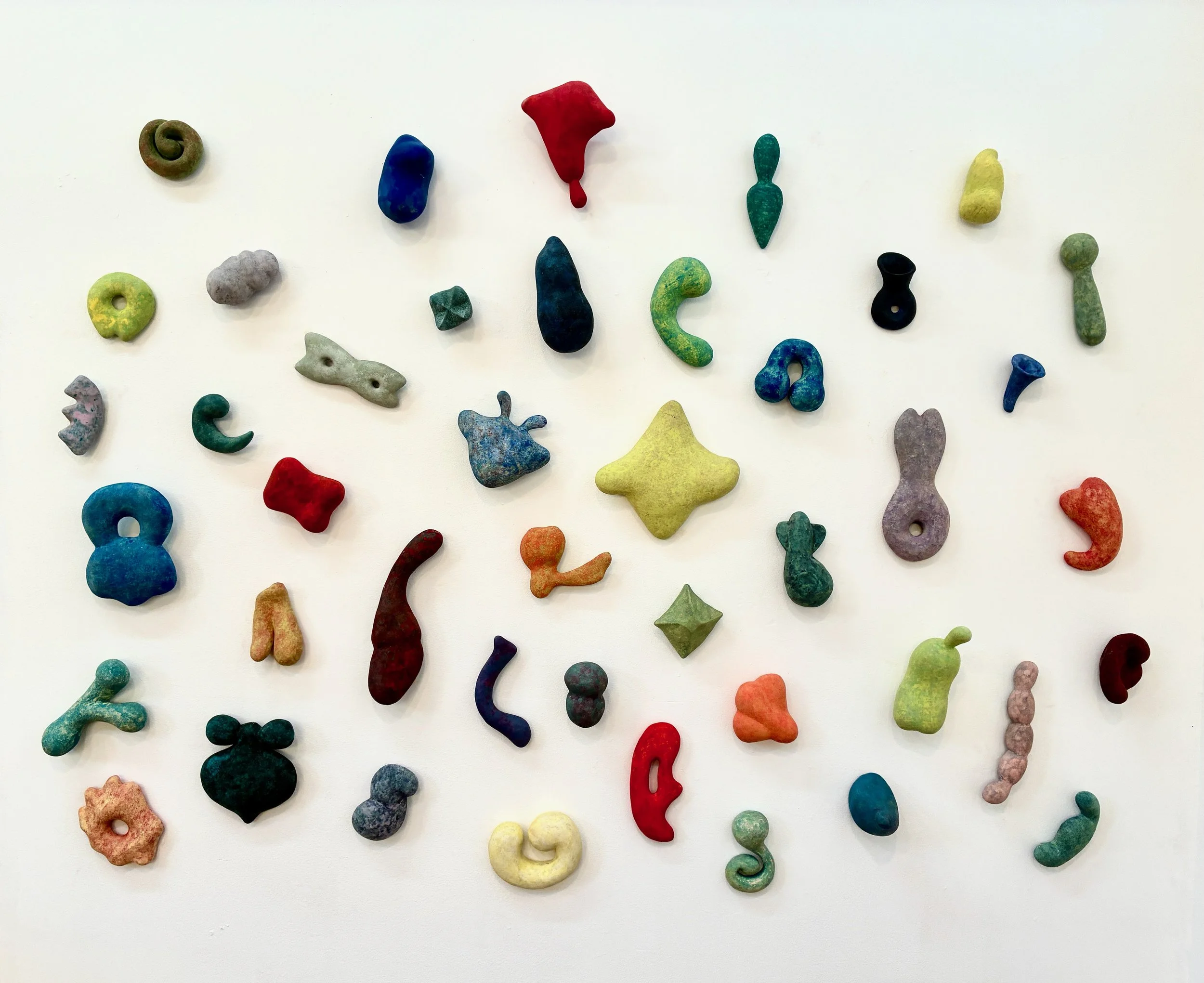 Multiple small ceramic sculptures hung on the wall as a group