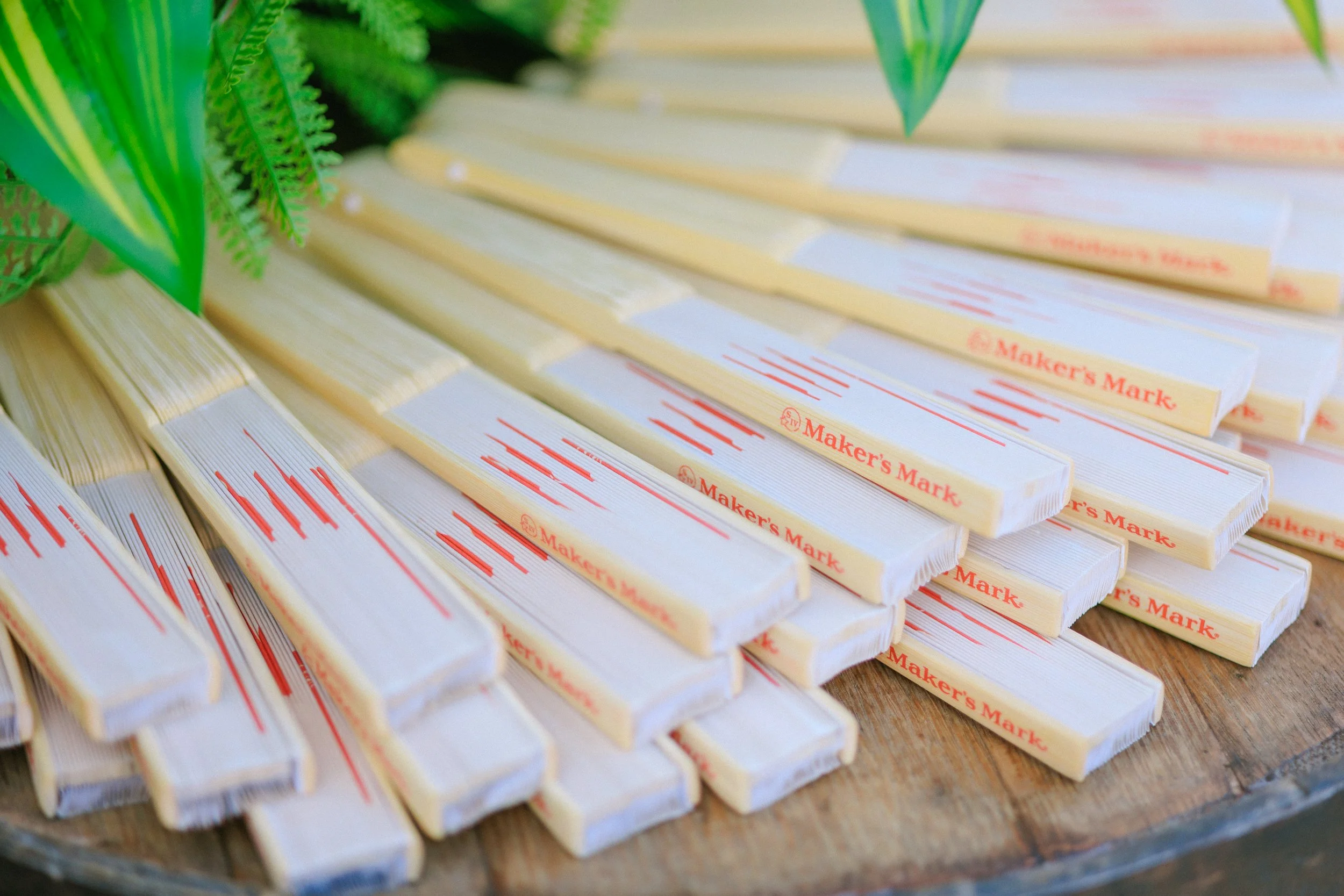 Stacks of Maker's Mark whiskey cheese snacks arranged on a wooden surface with green decorative leaves nearby.