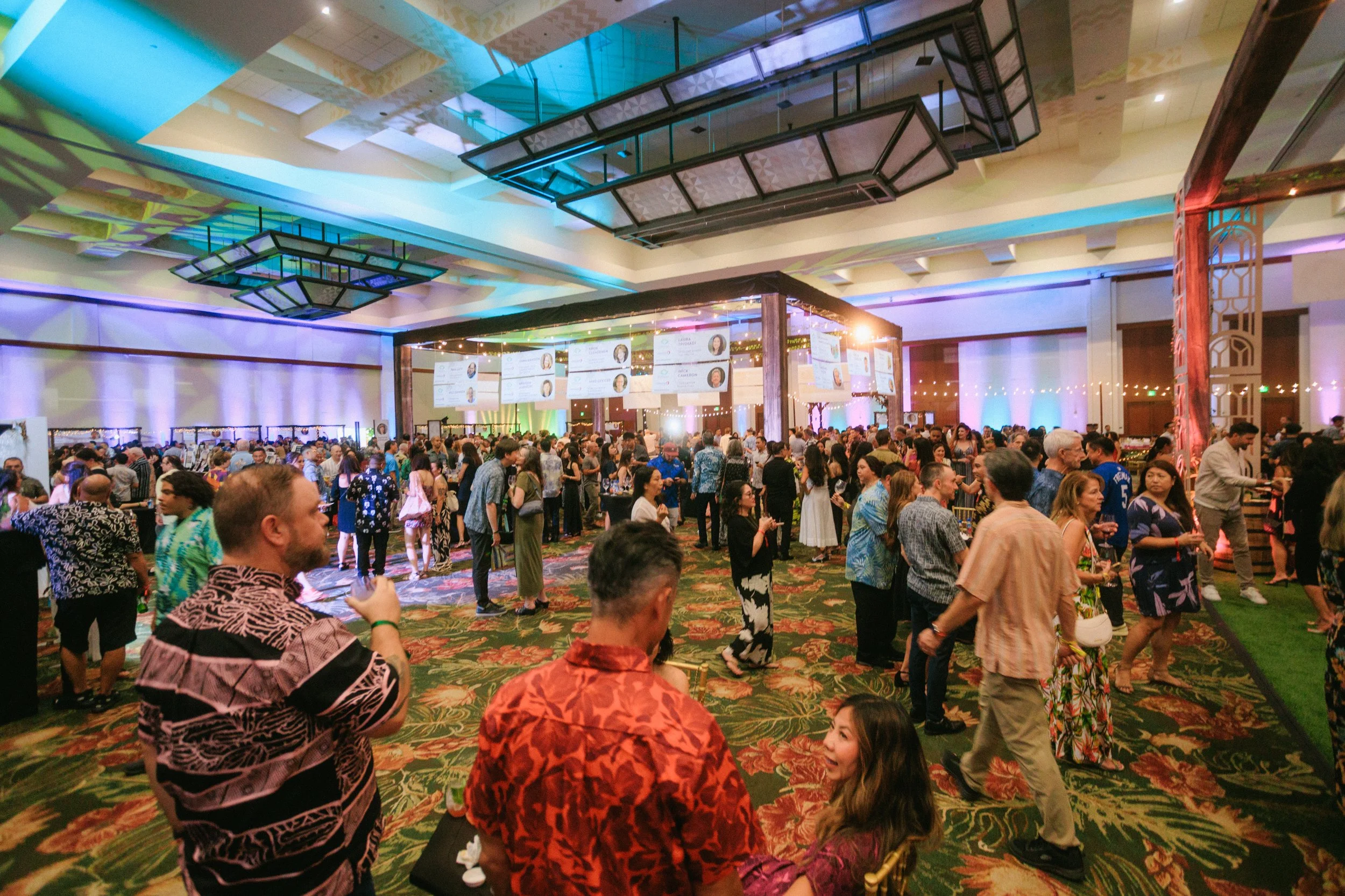 People attending a lively event or conference in a large, decorated indoor venue with colorful lighting and patterned carpet.