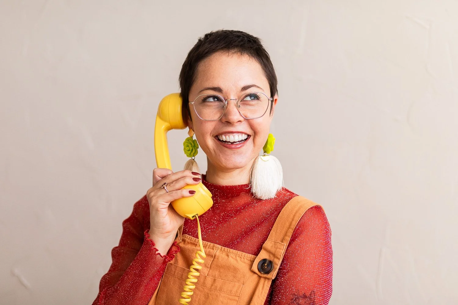 A woman against a white wall laughing and on a yellow telephone