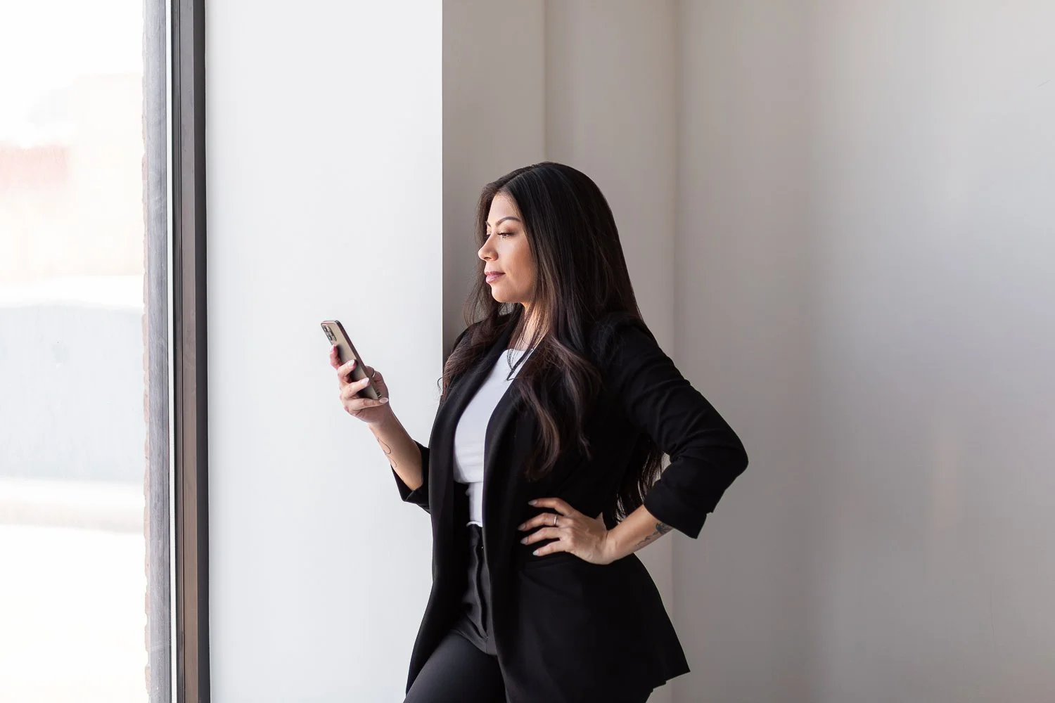A Chicago realtor stands in a window on her phone wearing professional clothing