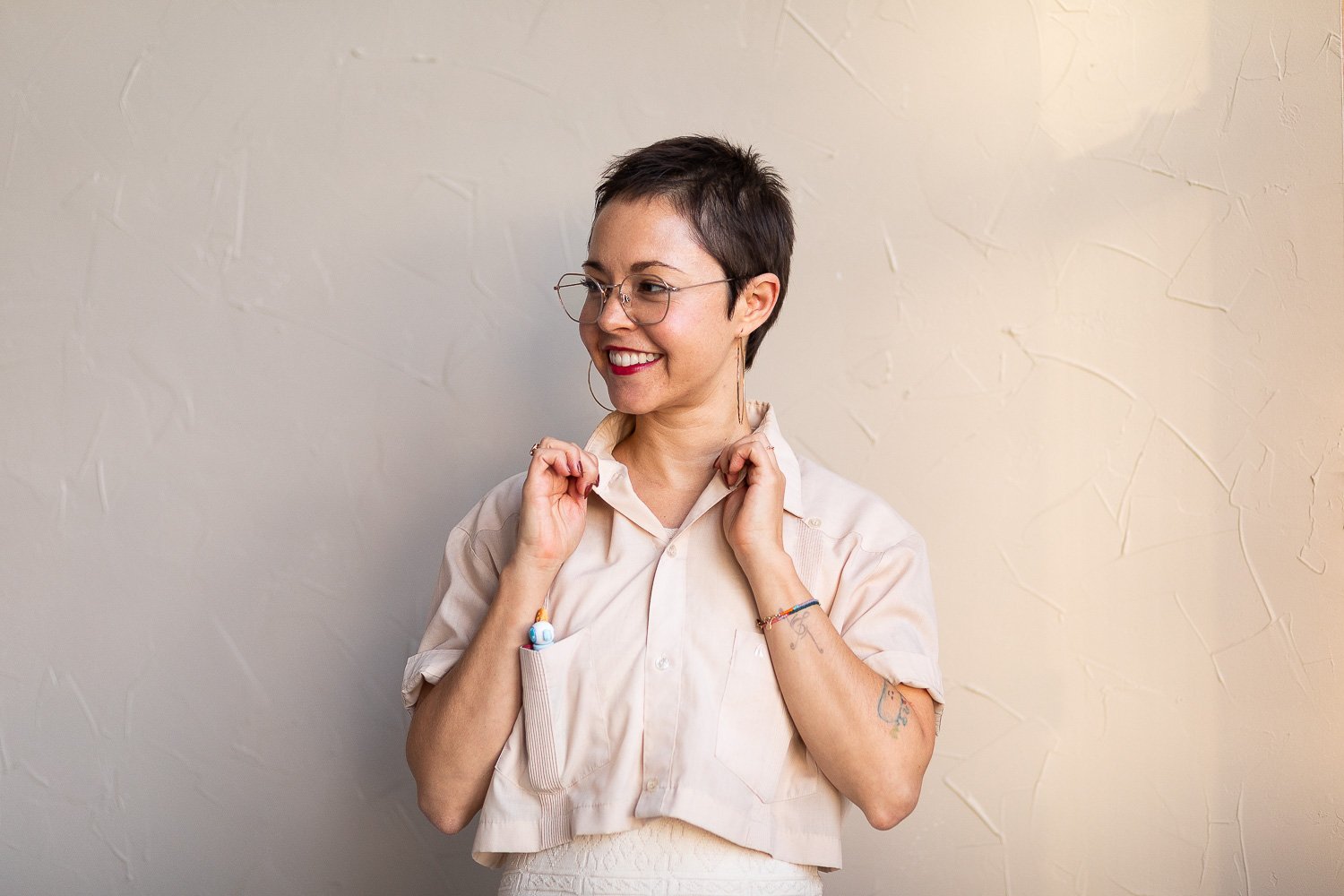 A woman popping the collar of her tan shirt and looking off into the distance