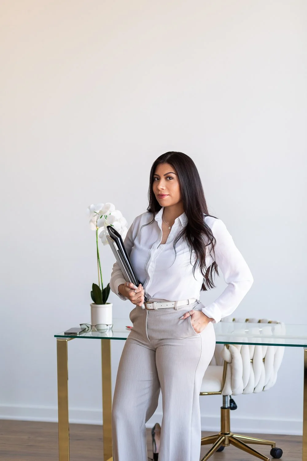 A realtor in professional clothing leans against a modern desk in a white room