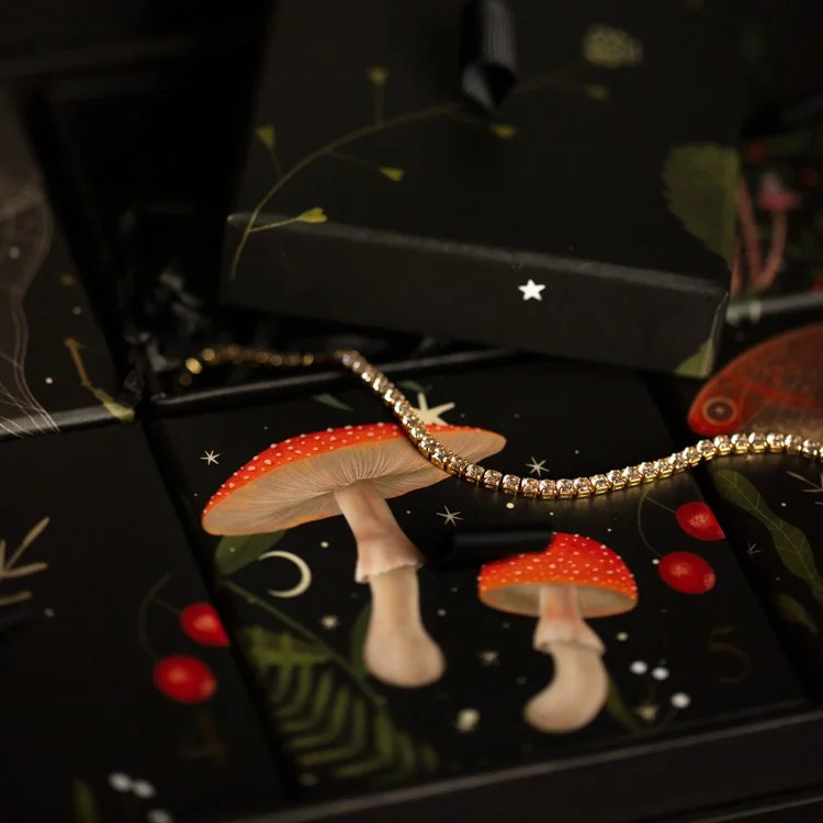 CZ encrusted choker necklace lays on top of Advent Calendar box designed by Local Eclectic. There are mushrooms, moons, stars, and floral designs on the box.