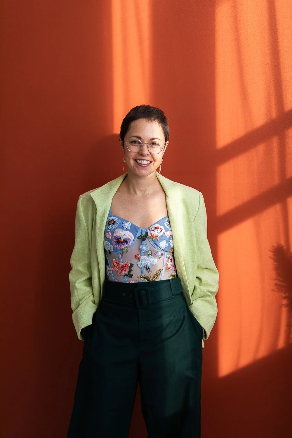 A woman with short hair against a red wall in bright, colorful business wear