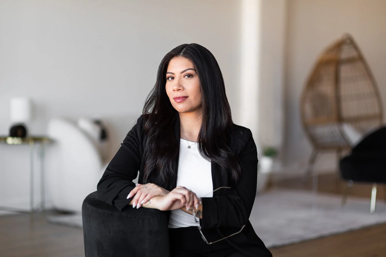 A realtor sits on a chair in a modern white room holding a pair of glasses
