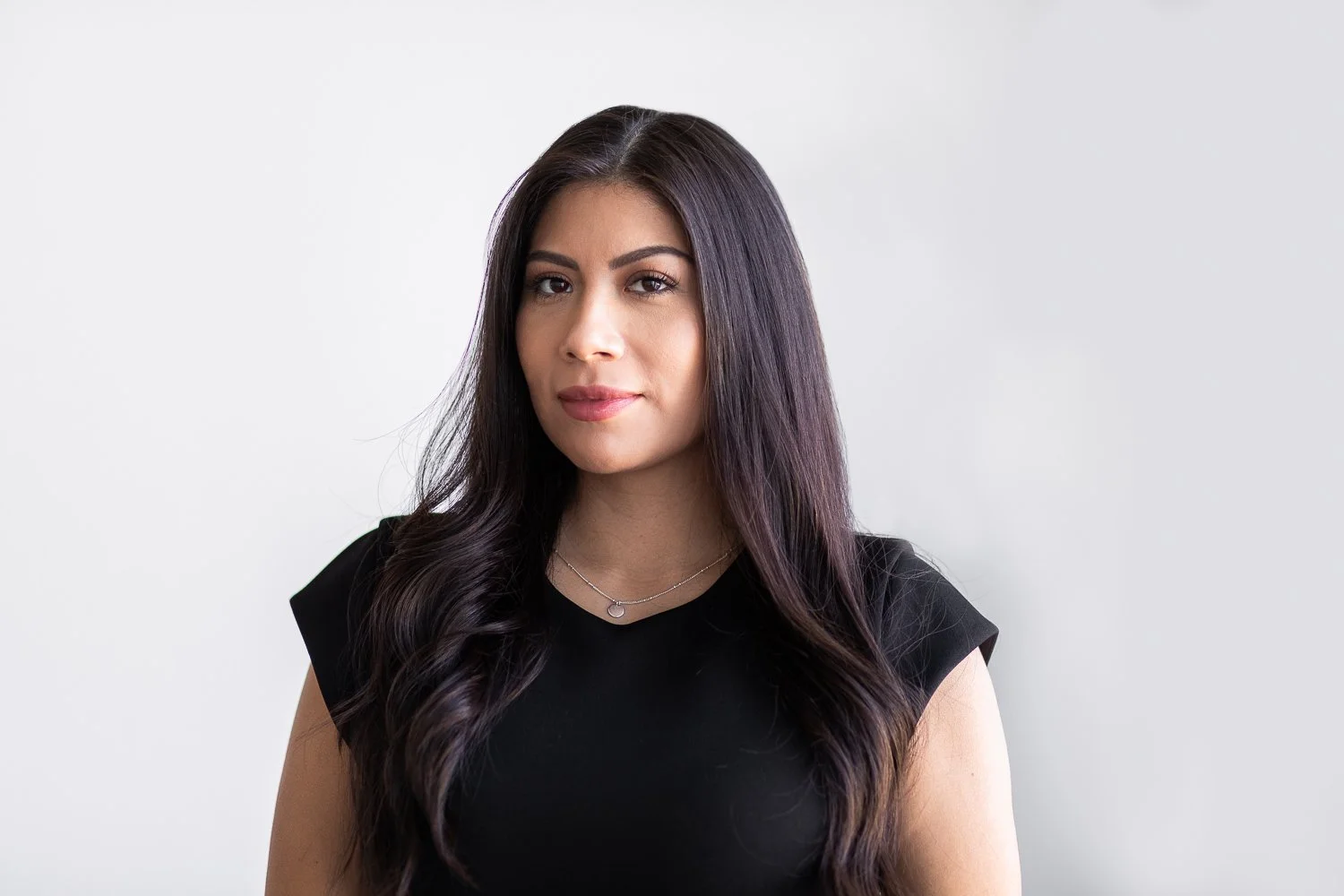 A realtor against a white wall with long dark hair