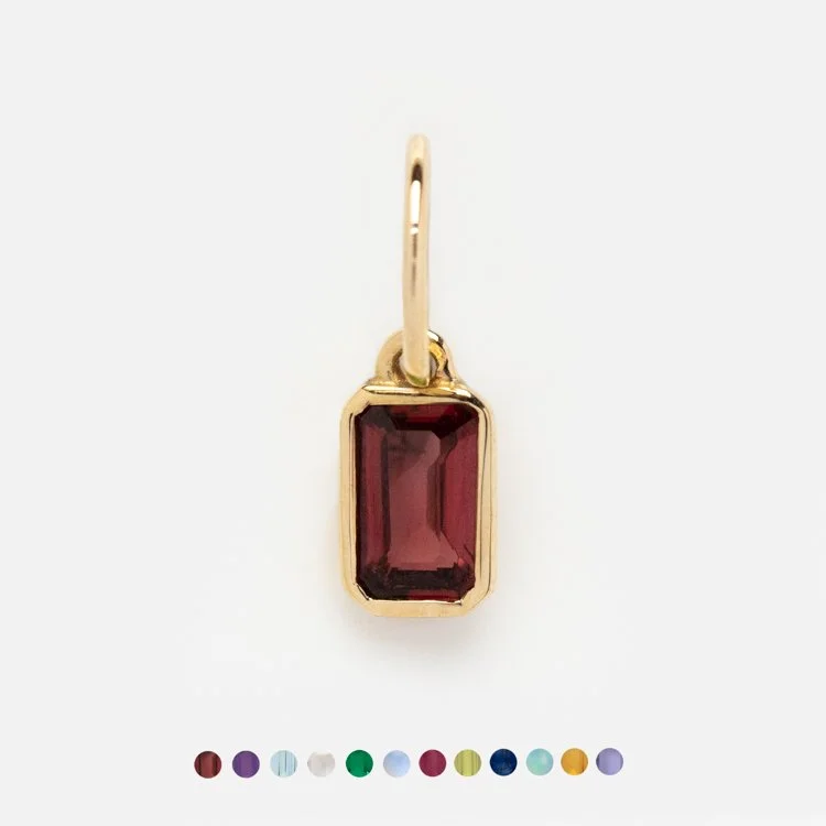 Close up view of a yellow gold charm that goes onto a charm necklace. The charm features a large red garnet stone in the center of a yellow gold square setting.