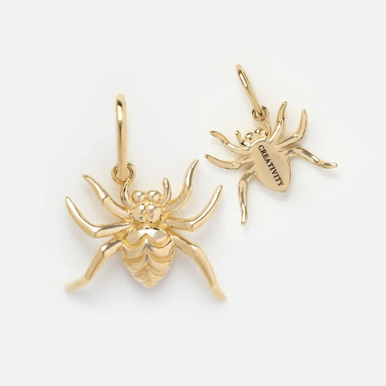 A view of the front and back of a yellow gold spider charm. The back of the charm says "Creativity."