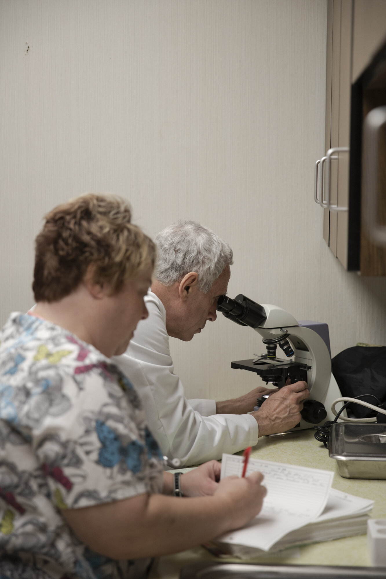 Dr. Moughon looks through the microscope while his receptionist, Tina Jones, prepares patient data.