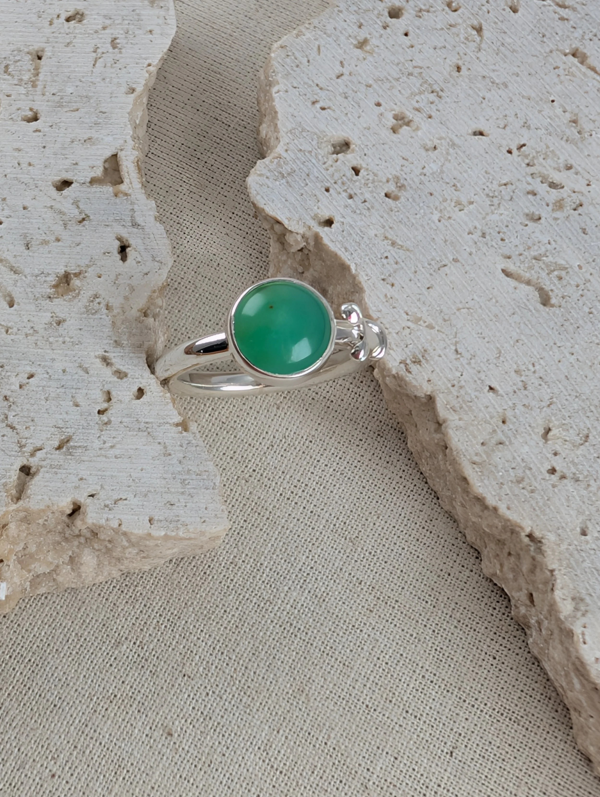Handcrafted silver ring with a round green chrysoprase gemstone and delicate botanical leaf details wrapping onto the band