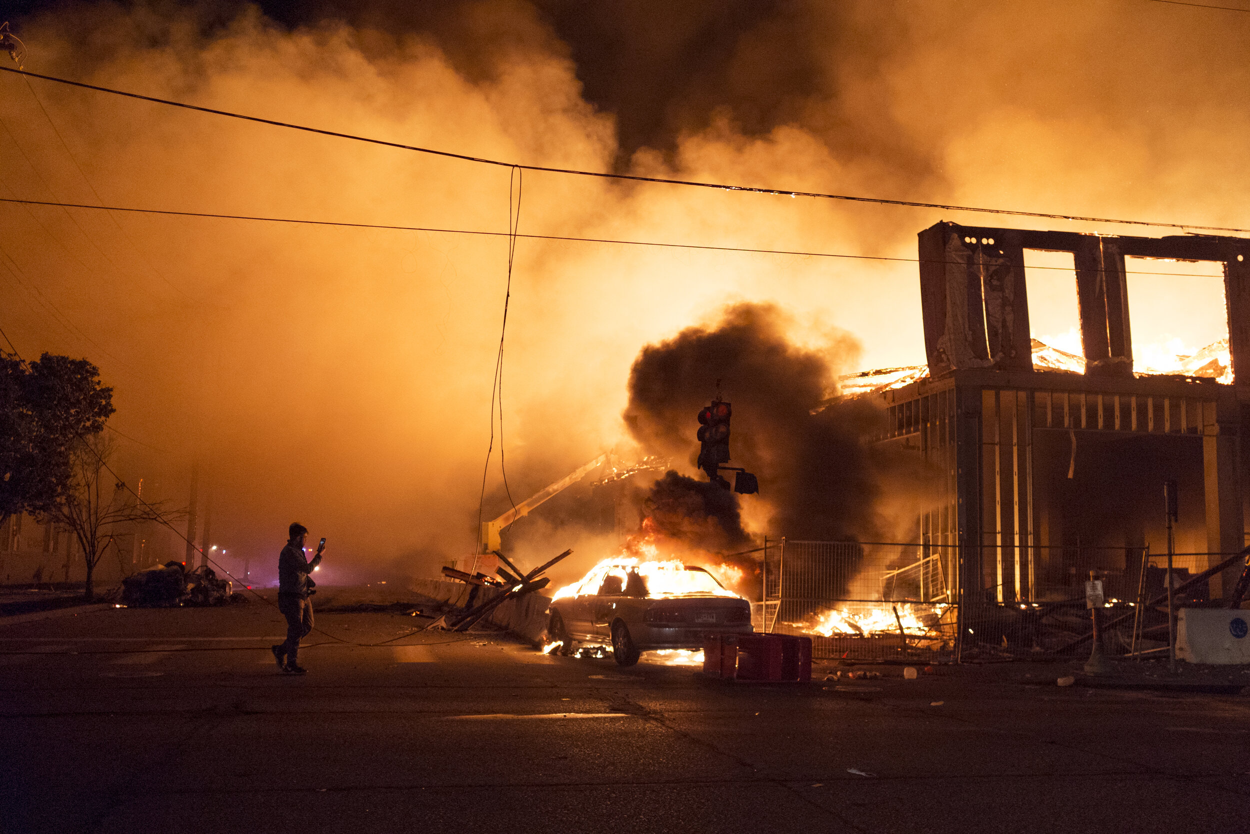  A bystander records on their phone while the remnants of an unfinished apartment complex burns near Minneapolis’ Third Police Precinct on Thursday, May 28th 2020. During the Uprising, several structures, stores and businesses were targets for arson 