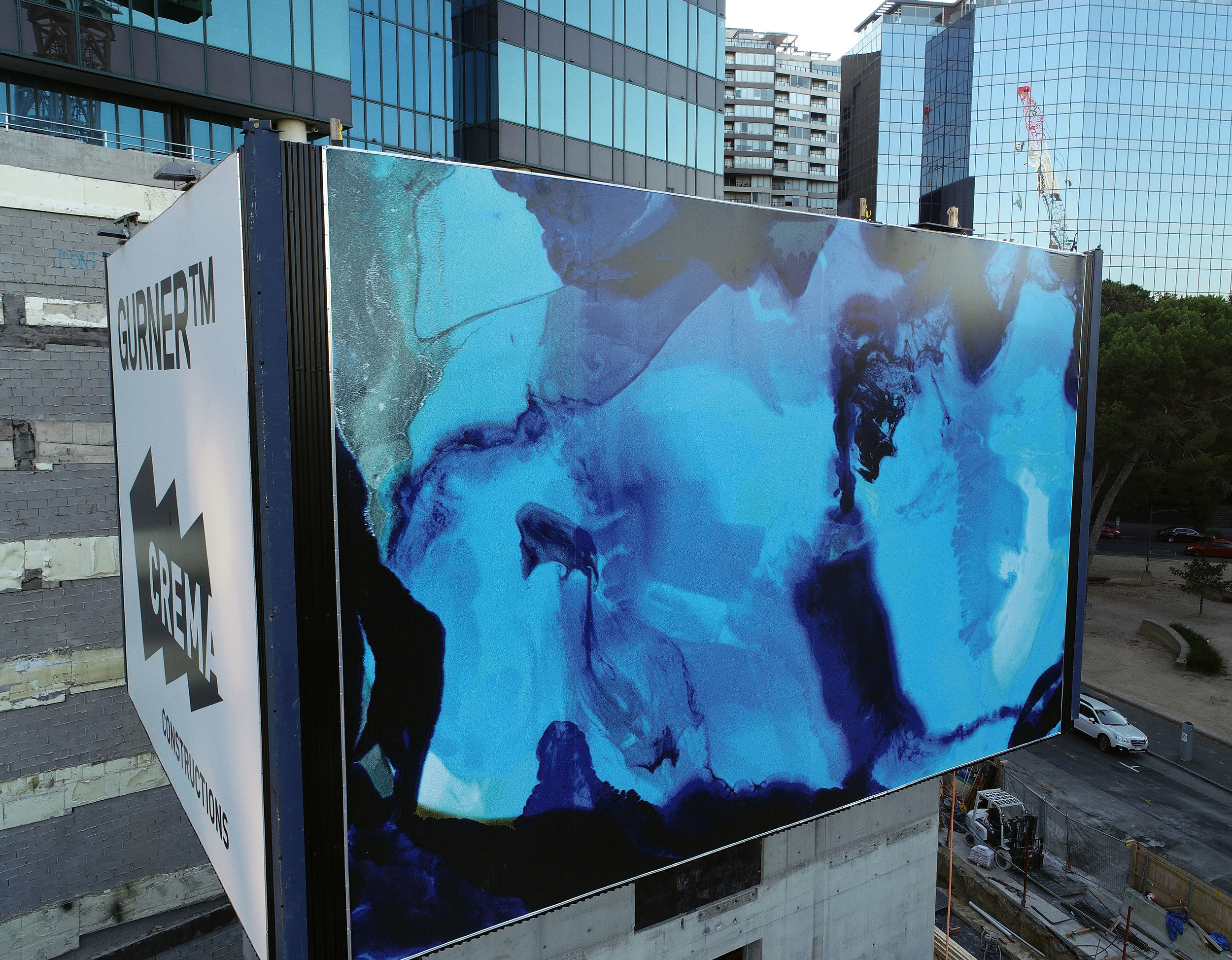 A large outdoor billboard features an abstract blue and black watercolor painting with the words 'GURNERT™ CREATIVE CONSTRUCTIONS' on the side.