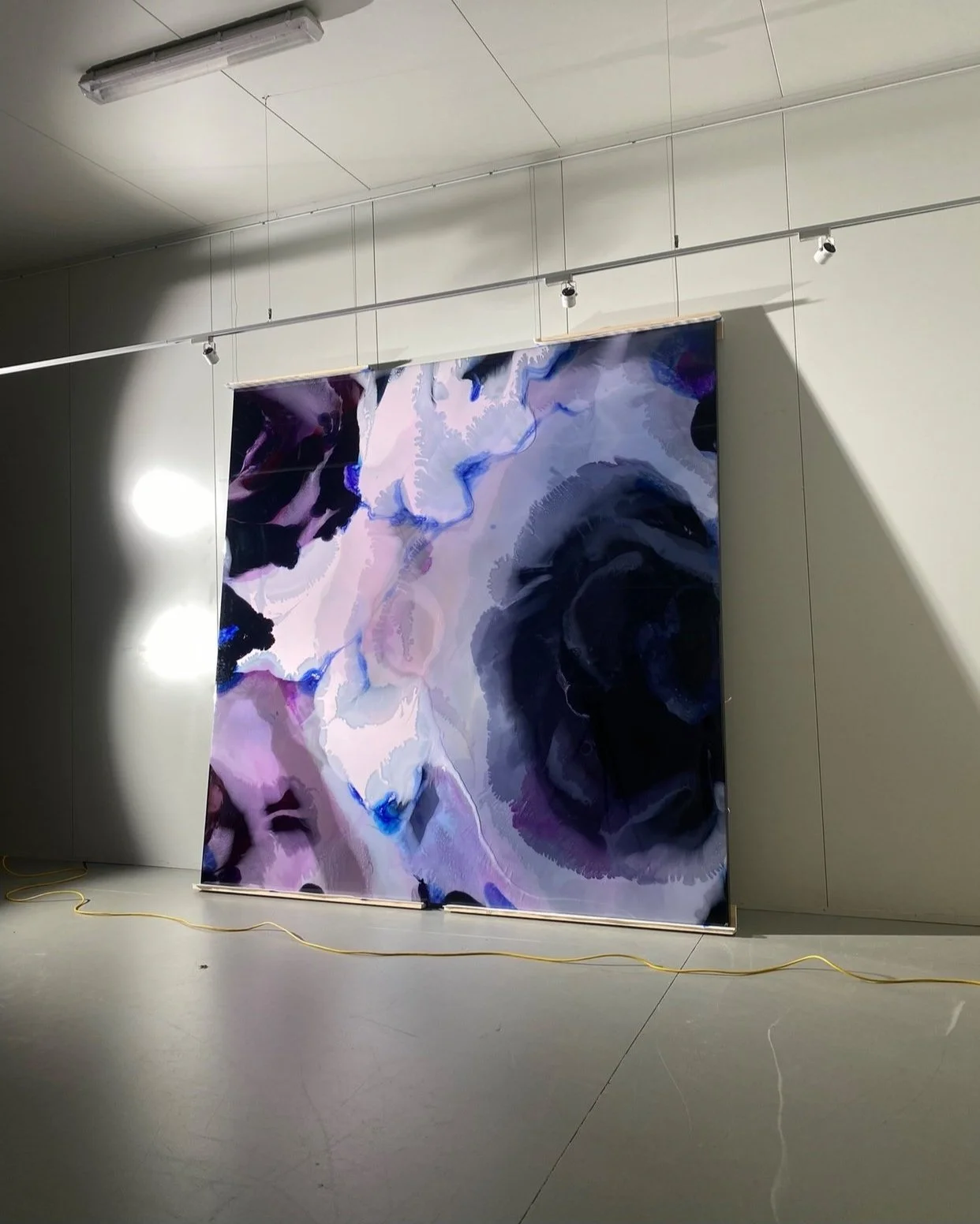 Large 3x3m abstract resin artwork with shades of purple, pink, blue, and black hanging resembling a black rose on a gallery wall, illuminated by ceiling lights.