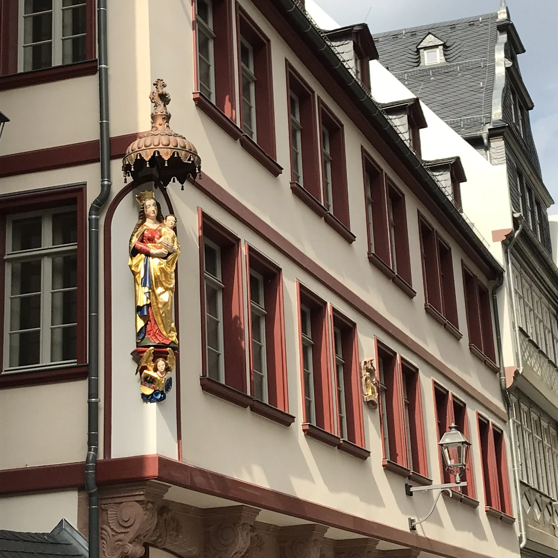 Hinter dem Lämmchen , Frankfurt new old town, with a decorative Madonna and child and crest on the wall, featuring multiple windows with red frames, a street lamp, and an ornate roof.