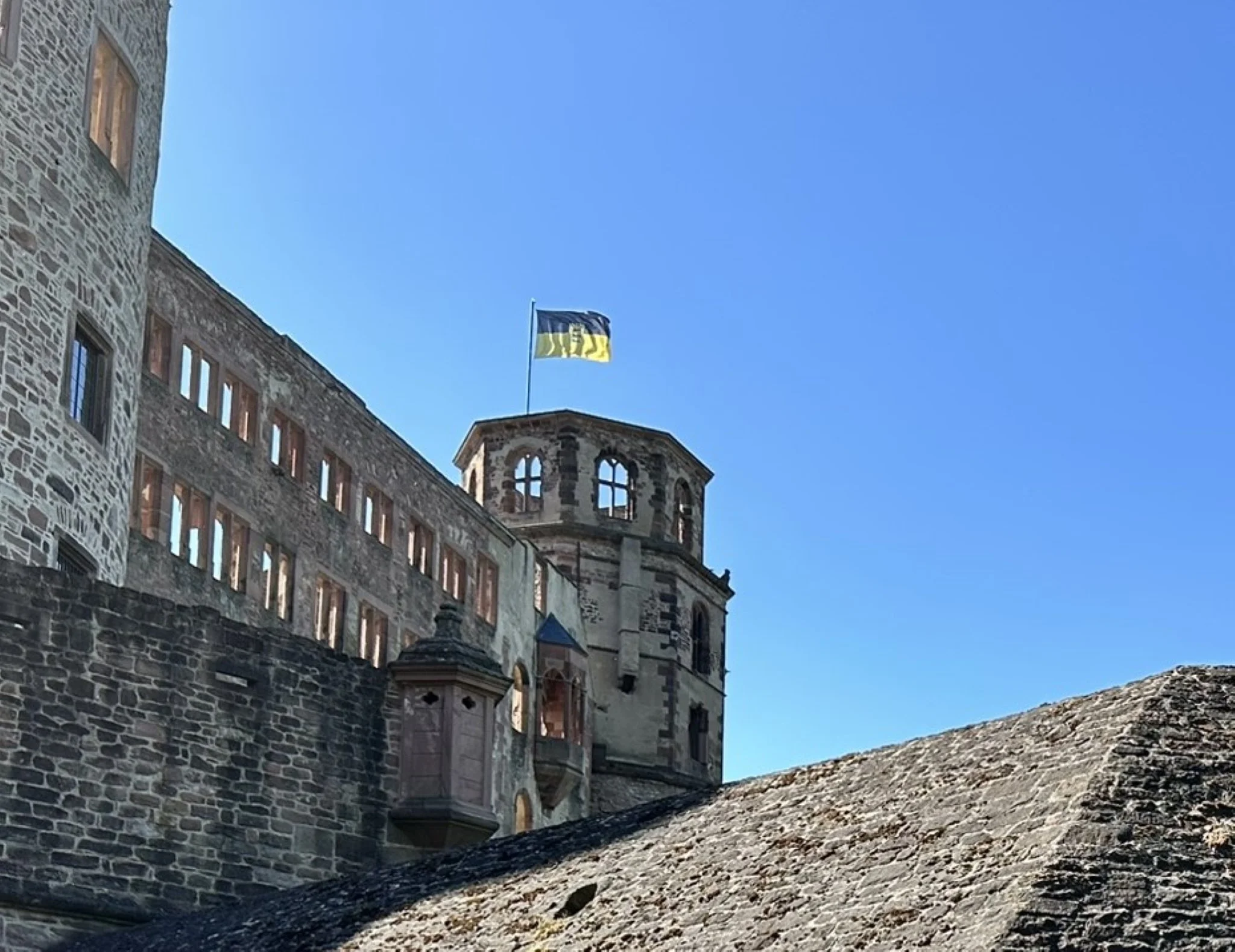 View of Heidelberg castle with a Baden Württemberg flag flying on top, set against a bright blue sky.