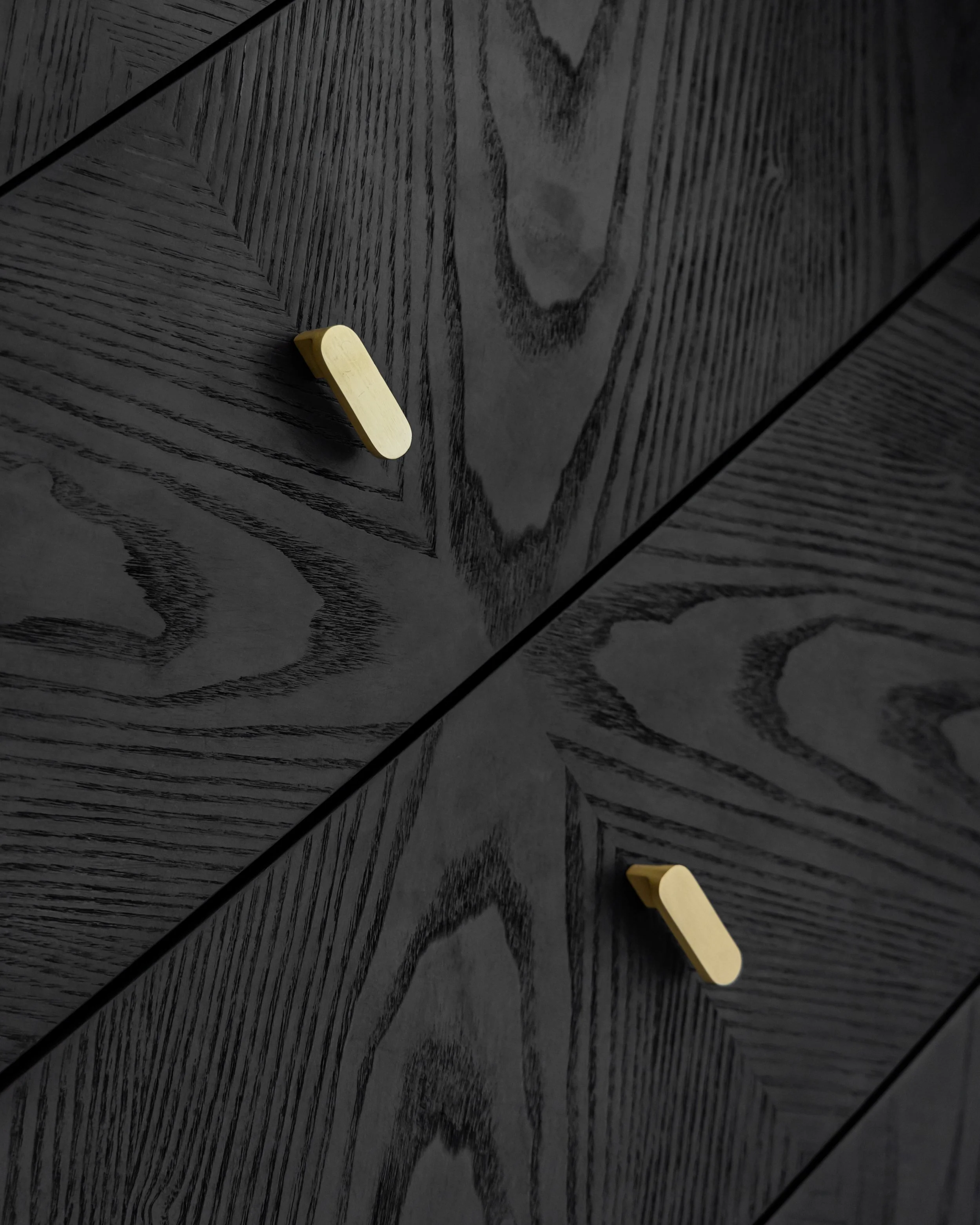 Close-up of a black wooden surface with wood grain pattern, featuring two light-colored drawer handles.
