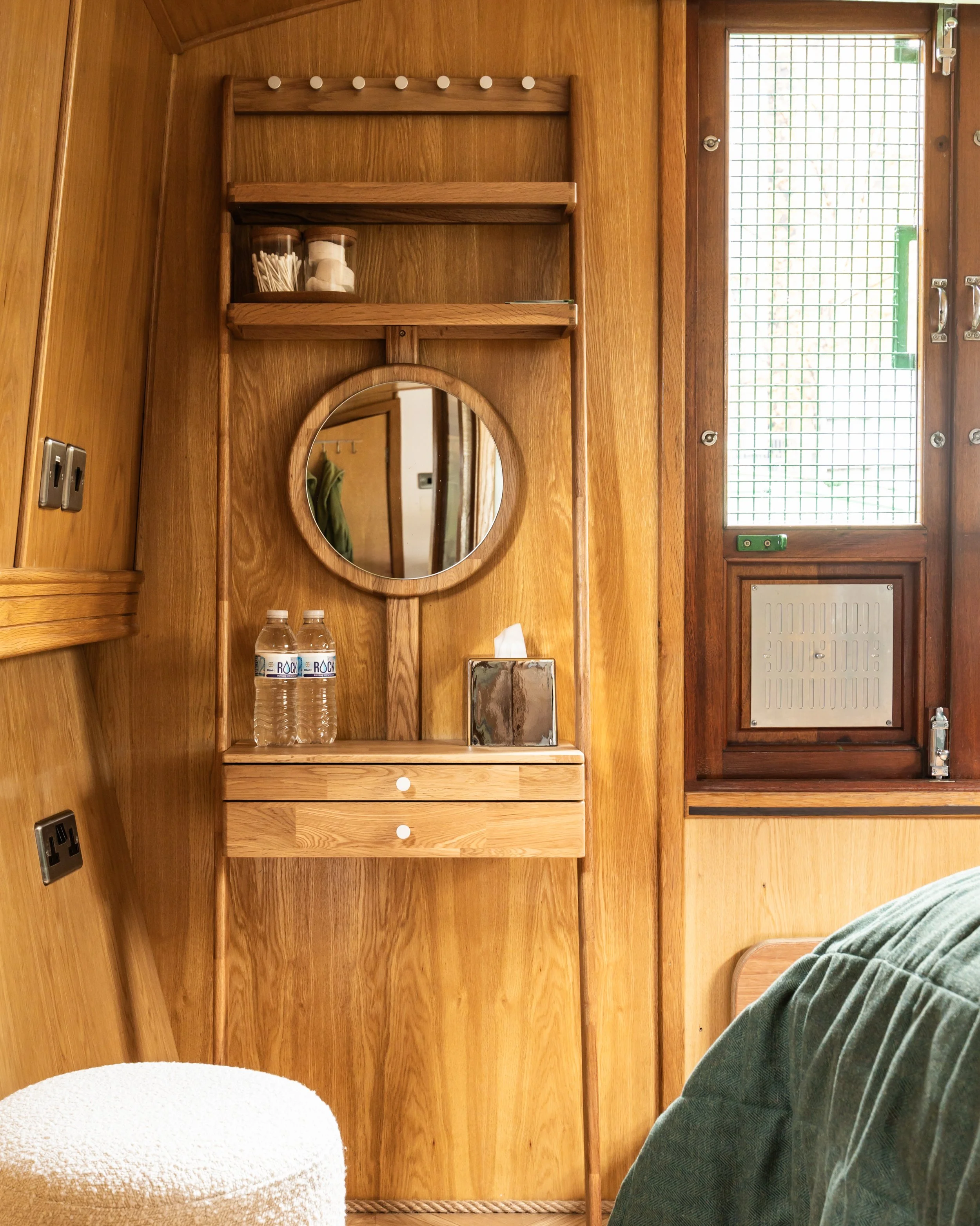 Wood-paneled wall with small shelf, round mirror, tissue box, and two water bottles.